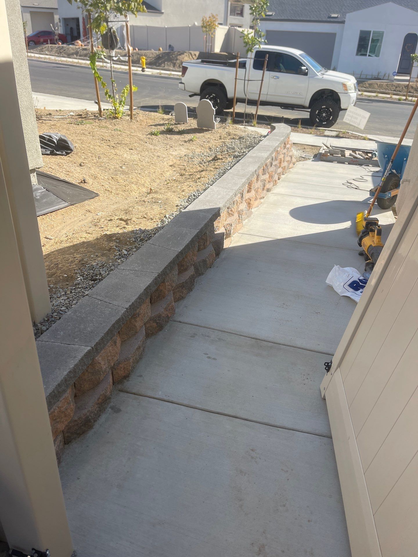 Concrete walkway leading to a house with a low retaining wall made of brown blocks and a white pickup truck parked nearby.