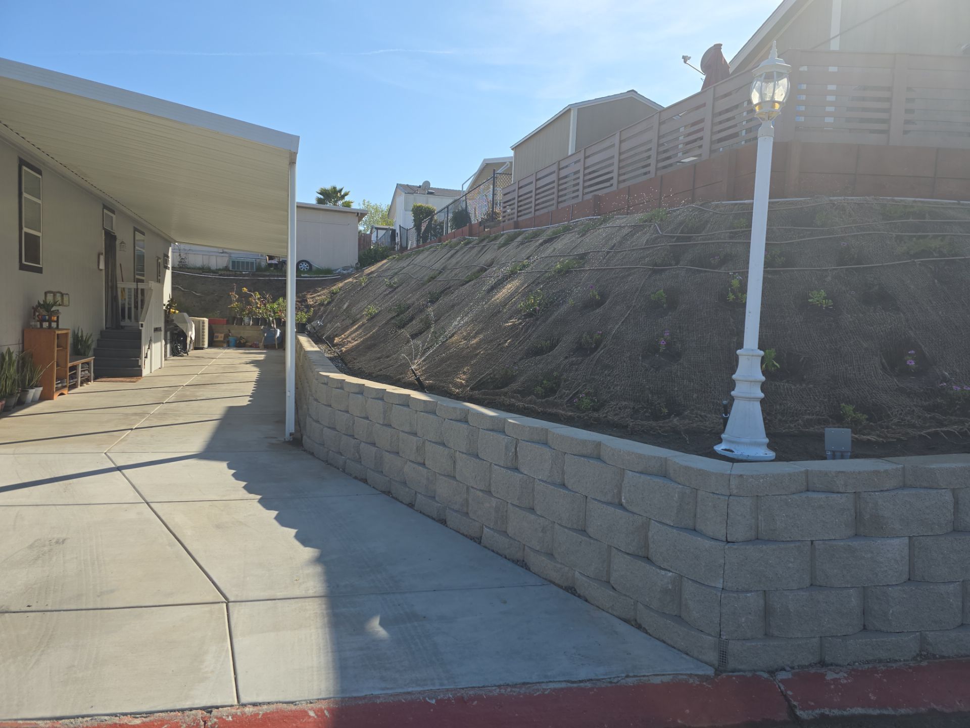 Concrete block retaining wall next to a concrete walkway, hillside with houses in background.