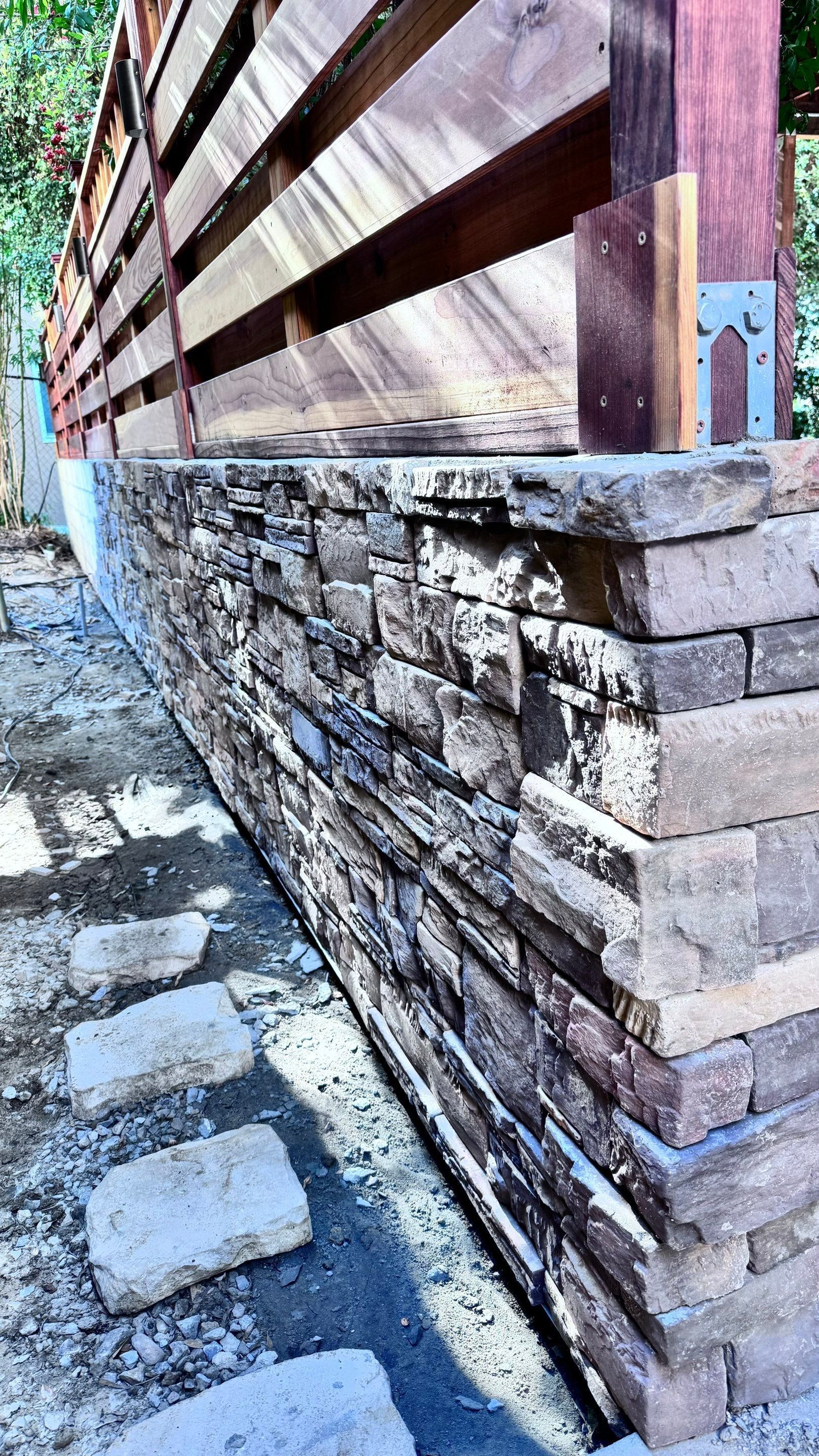 Stone wall with wood fence on top. Brick walkway in front.