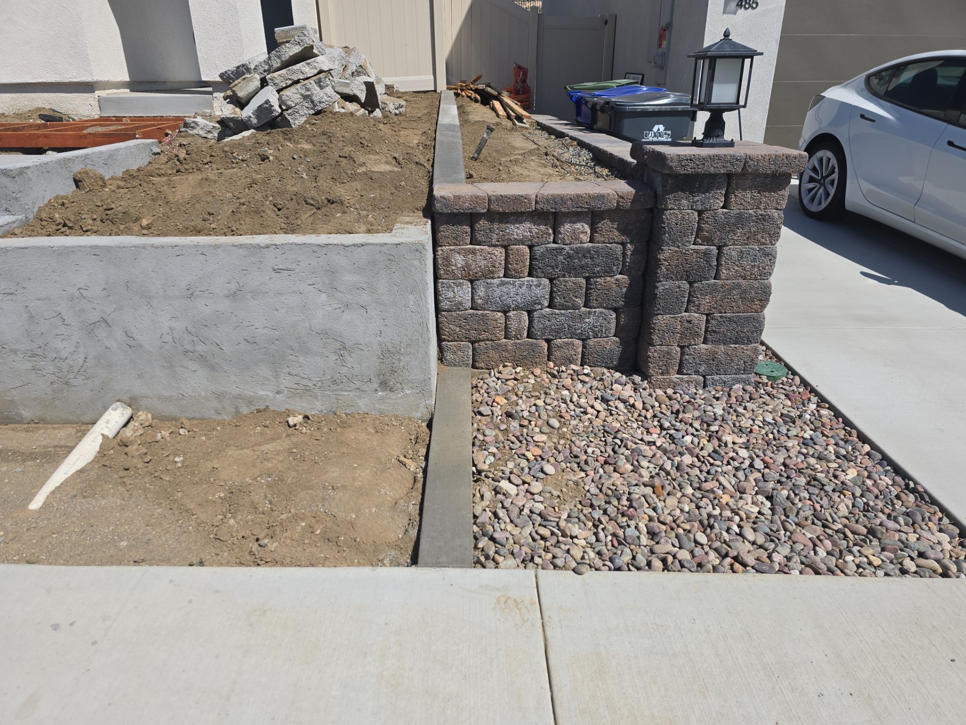 Exterior view of a house with concrete and brick retaining walls, gravel, and a car in the driveway.