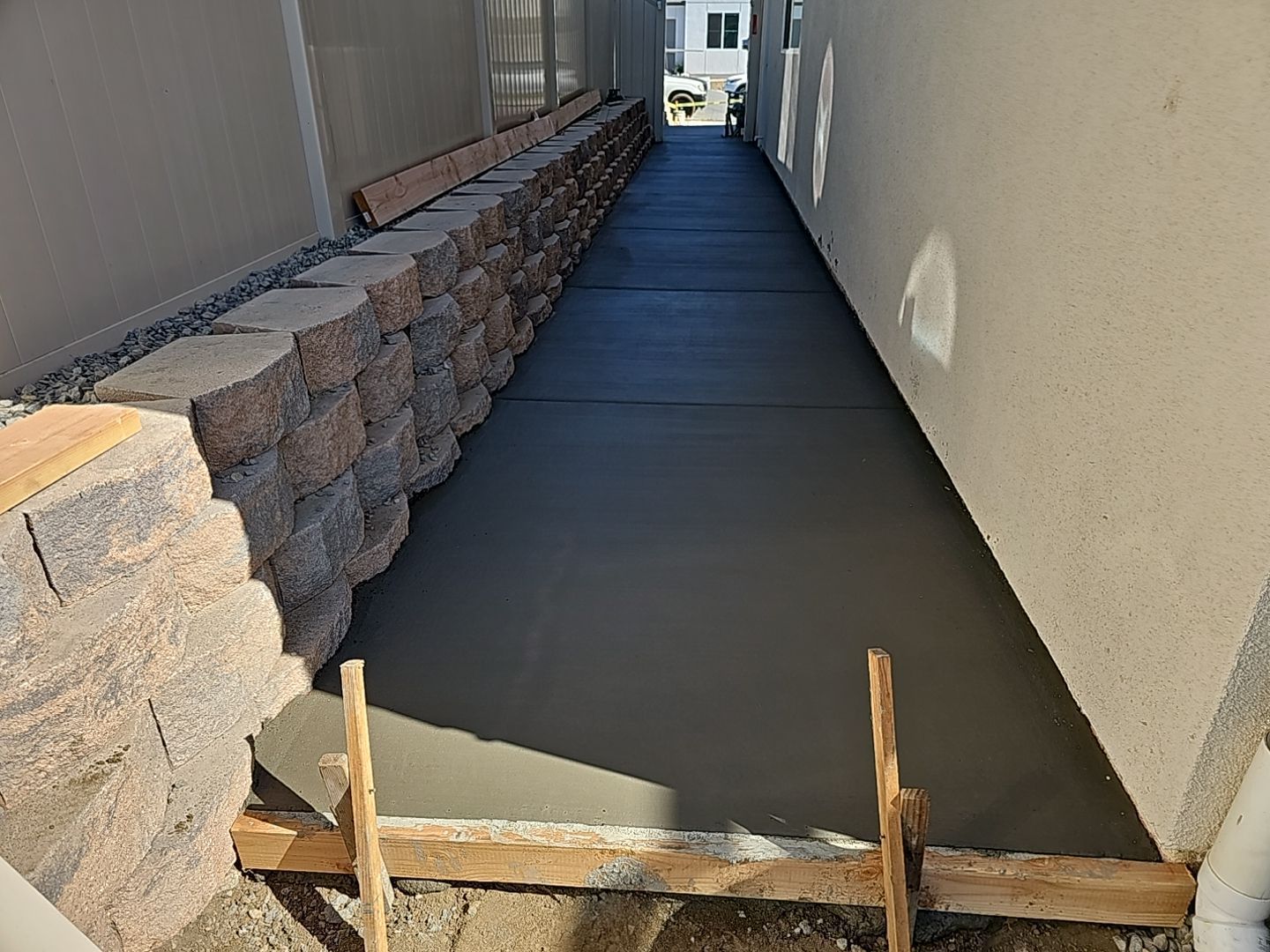 Newly poured concrete walkway between a retaining wall and building.