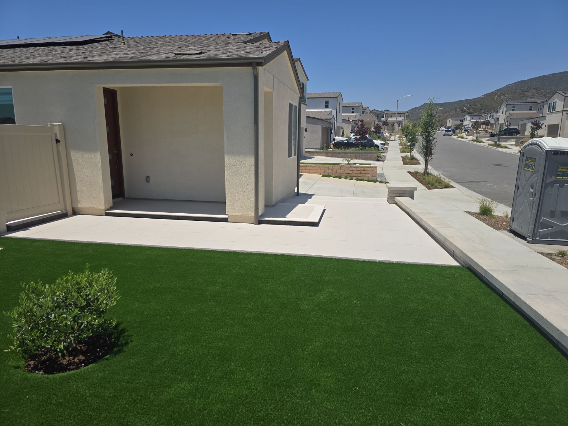 House exterior with artificial green lawn, concrete patio, and sidewalk in a sunny neighborhood.