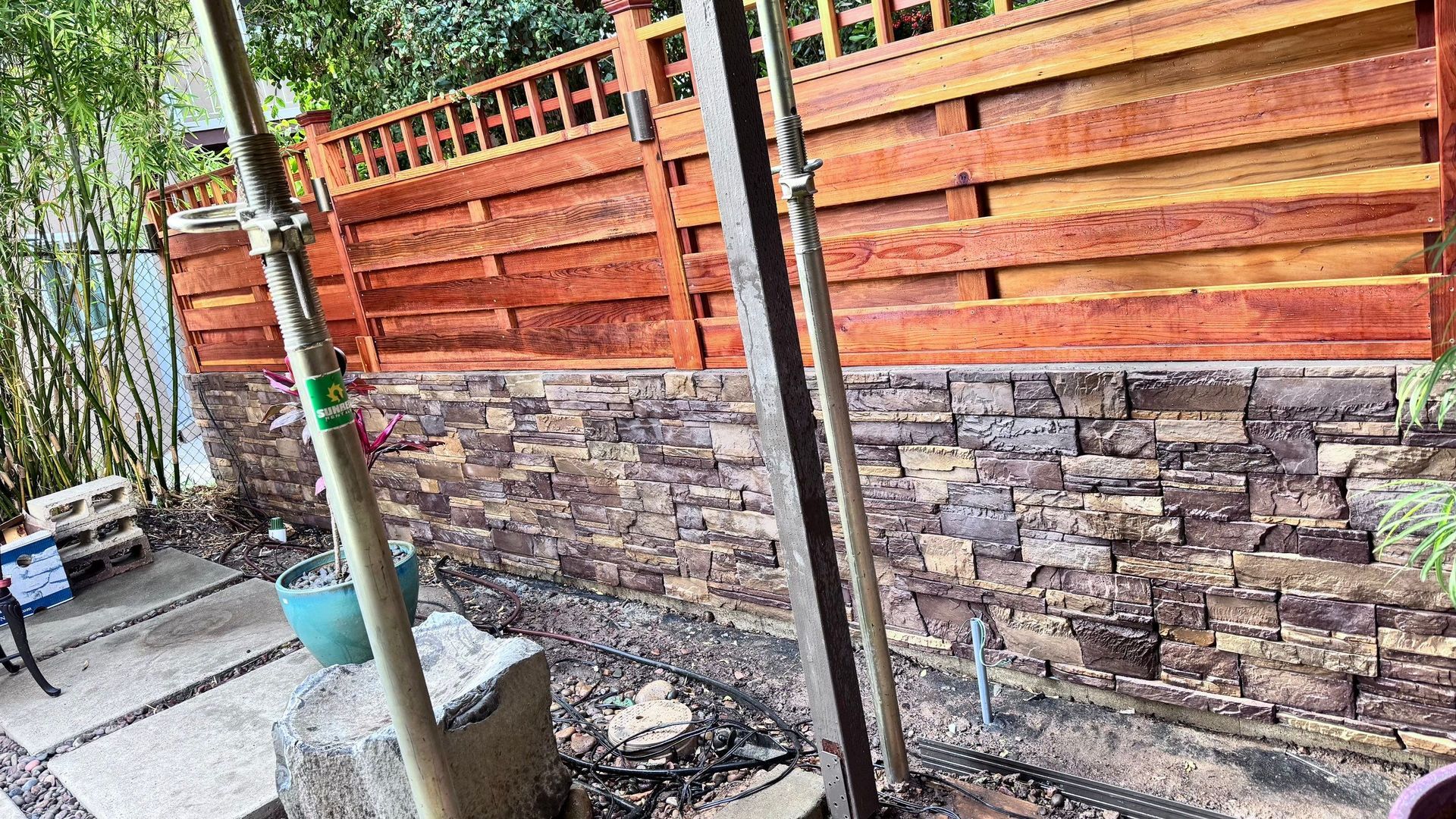 Stone wall with wooden fence above; support beams in foreground.