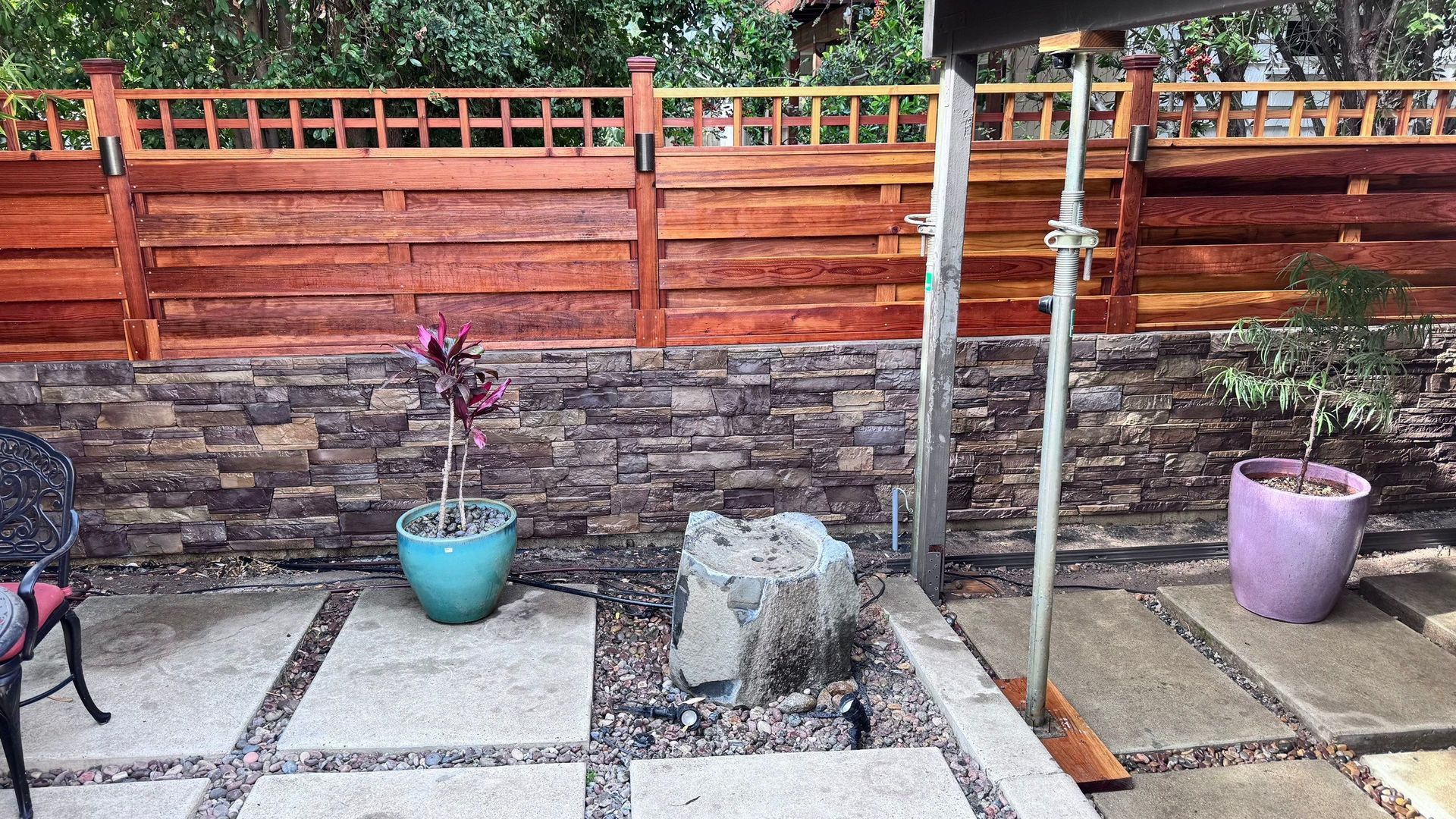 Outdoor patio with stone wall, wooden fence, potted plants, and concrete pavers.