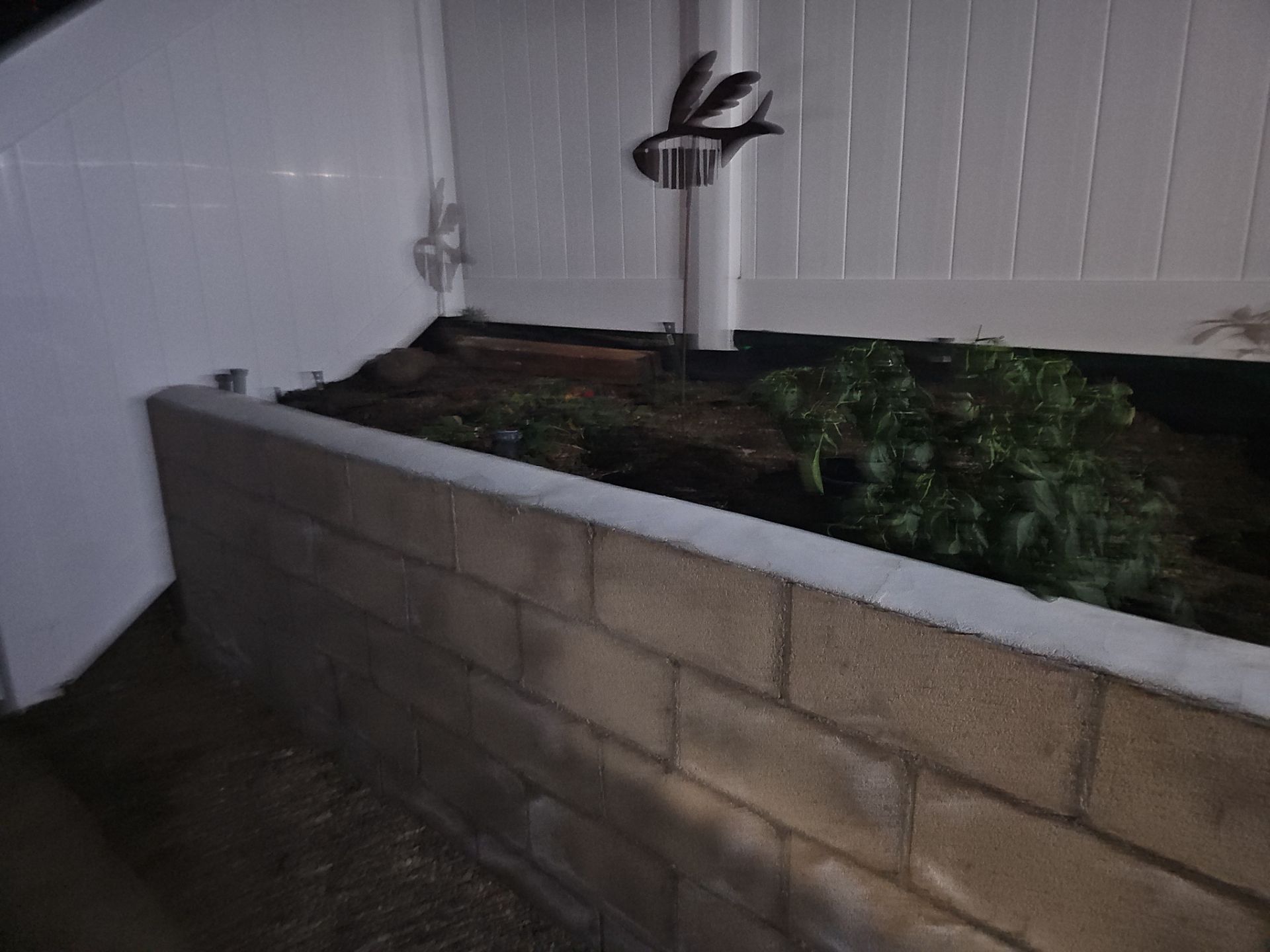 Raised garden bed with cinder block walls, plants, and a metal bird decoration.