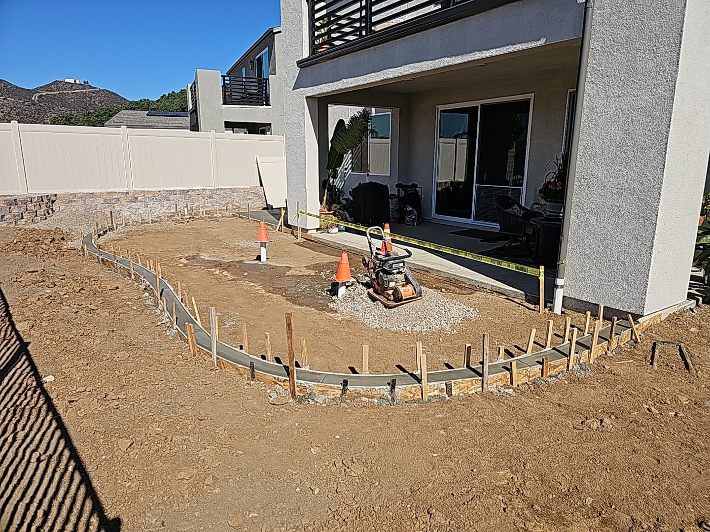 Construction site: Concrete curb forms outlined in dirt. House with sliding door in background.