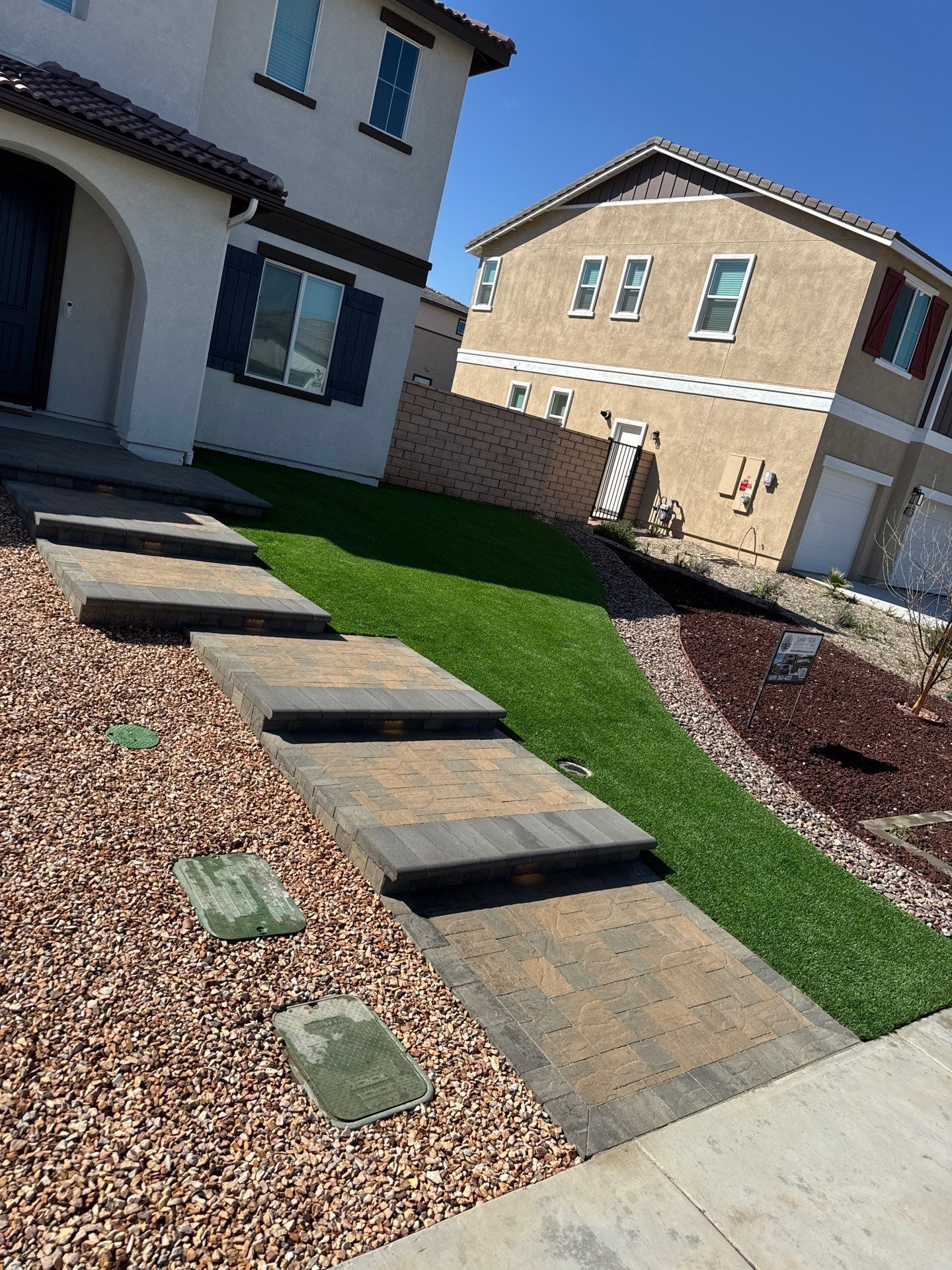 Stone steps leading up to a beige house with a green lawn and a neighbor's tan house.