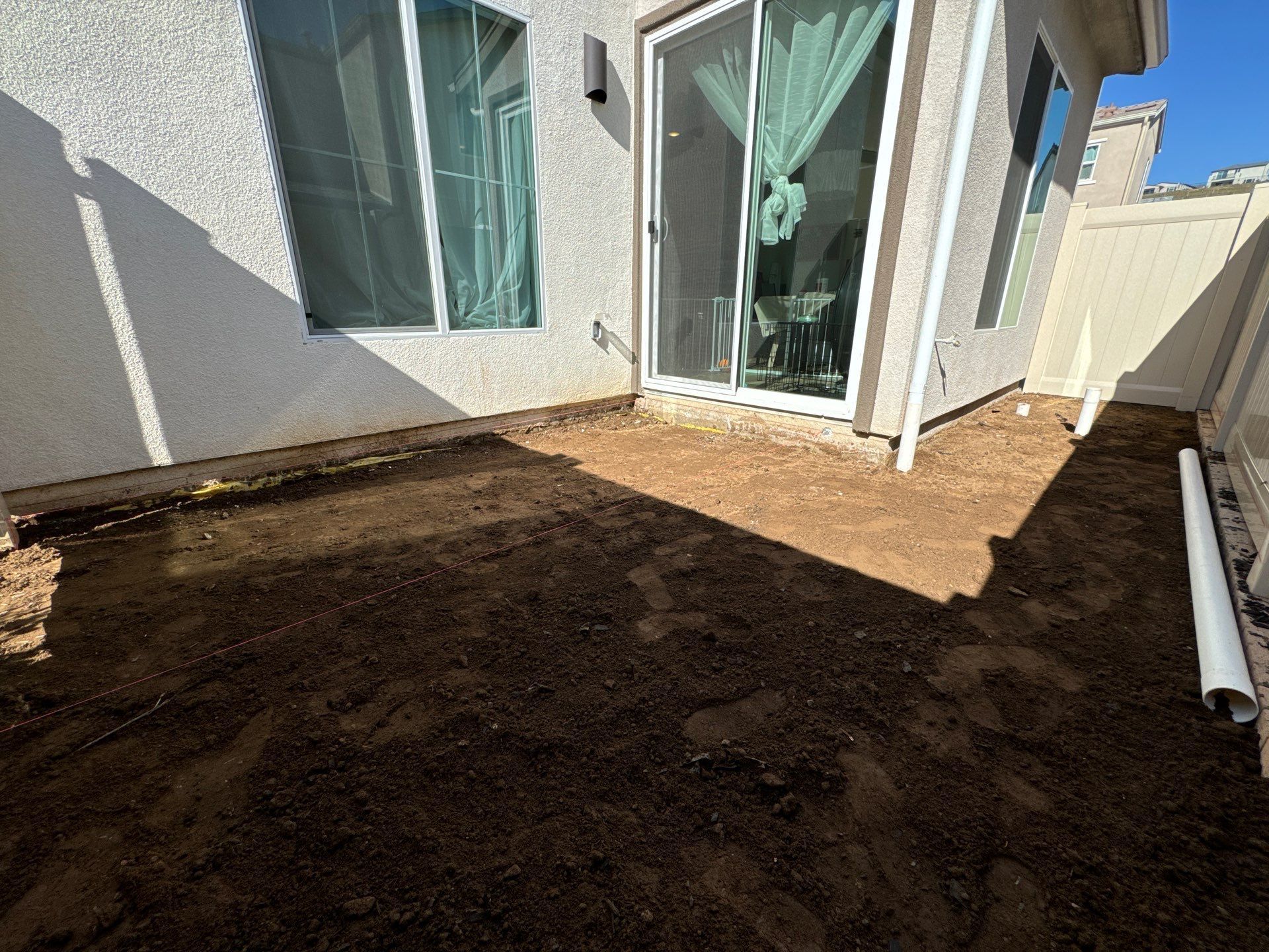 Backyard patio with dirt ground next to a white house with sliding glass door and window.