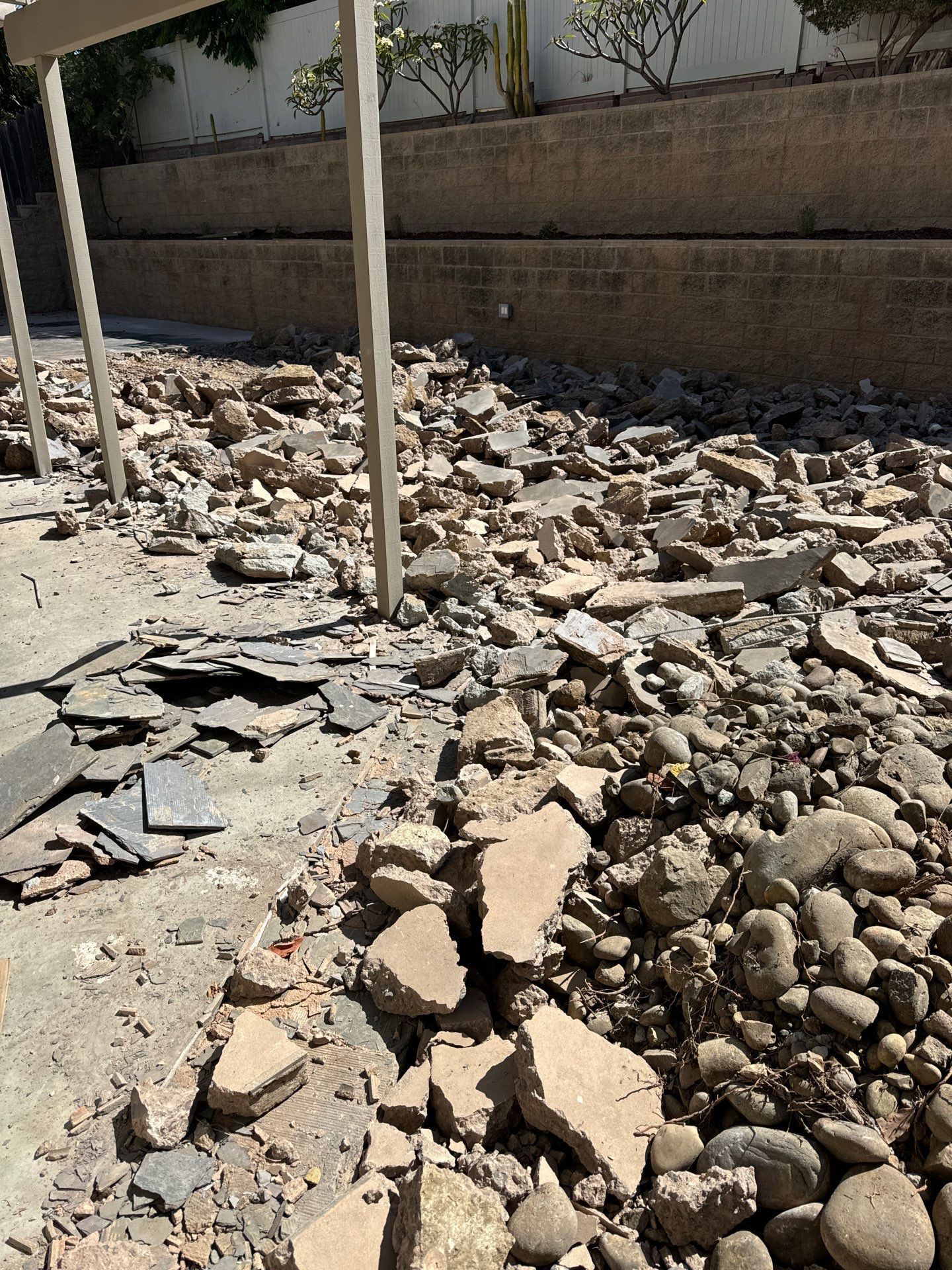 Debris-covered ground with broken concrete, rocks, and a retaining wall in the background.