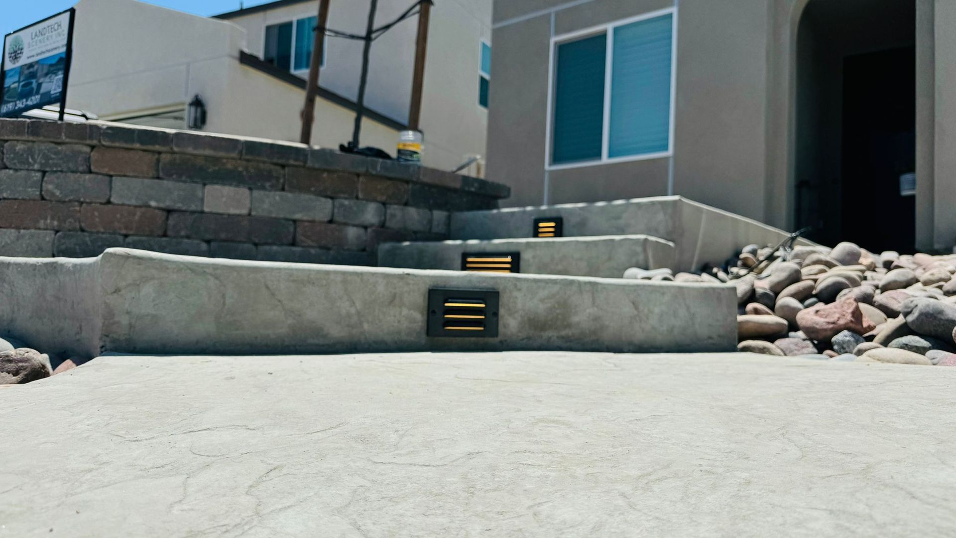 Concrete steps with built-in lights leading up to a beige house, with rocks and a retaining wall.