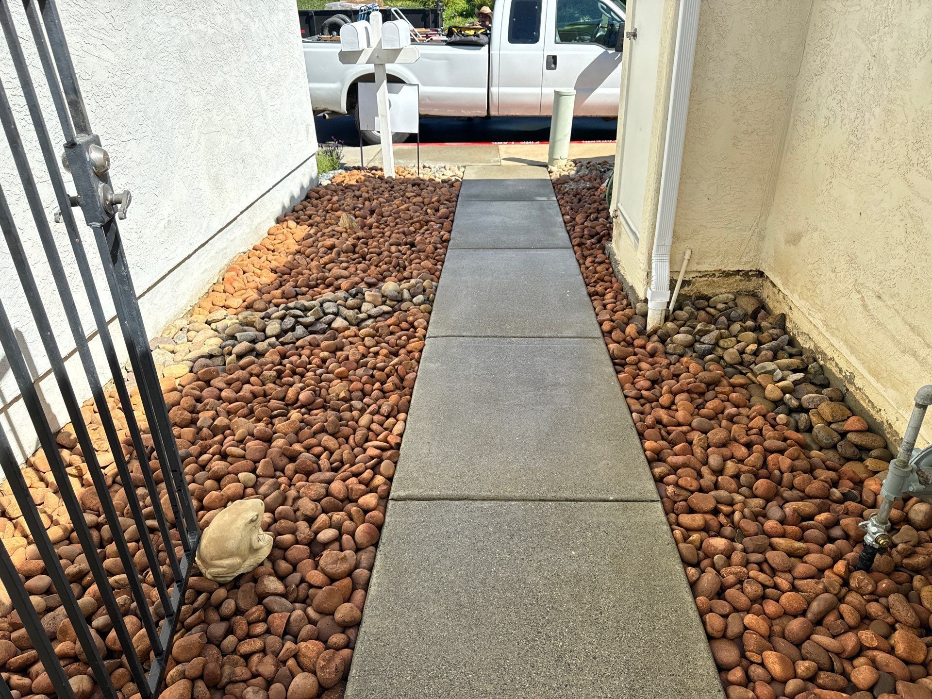 Pathway of gray paving stones flanked by brown river rock, with gate on left.