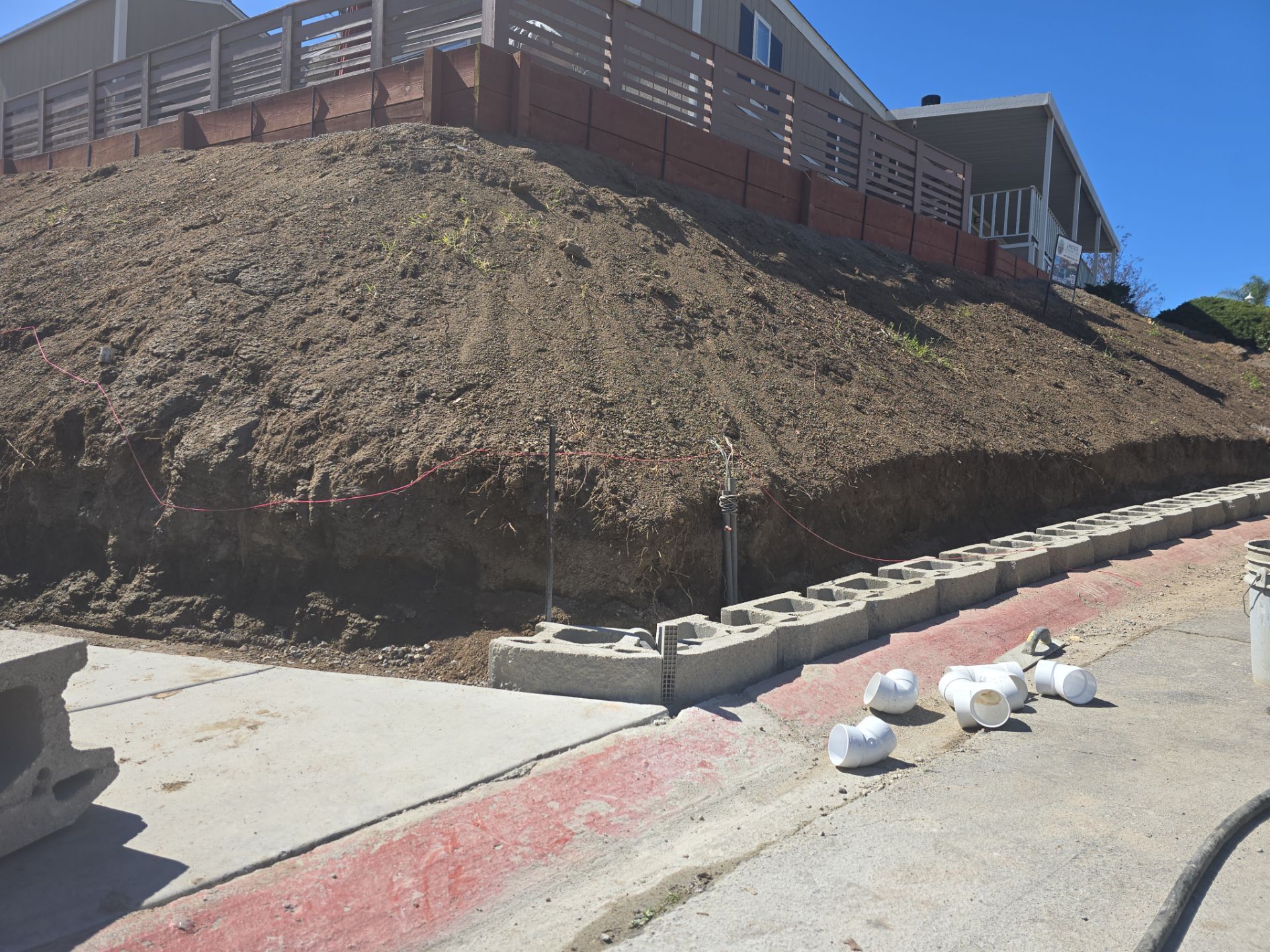 Sloped hillside with retaining walls and concrete path. PVC pipes sit on the path.