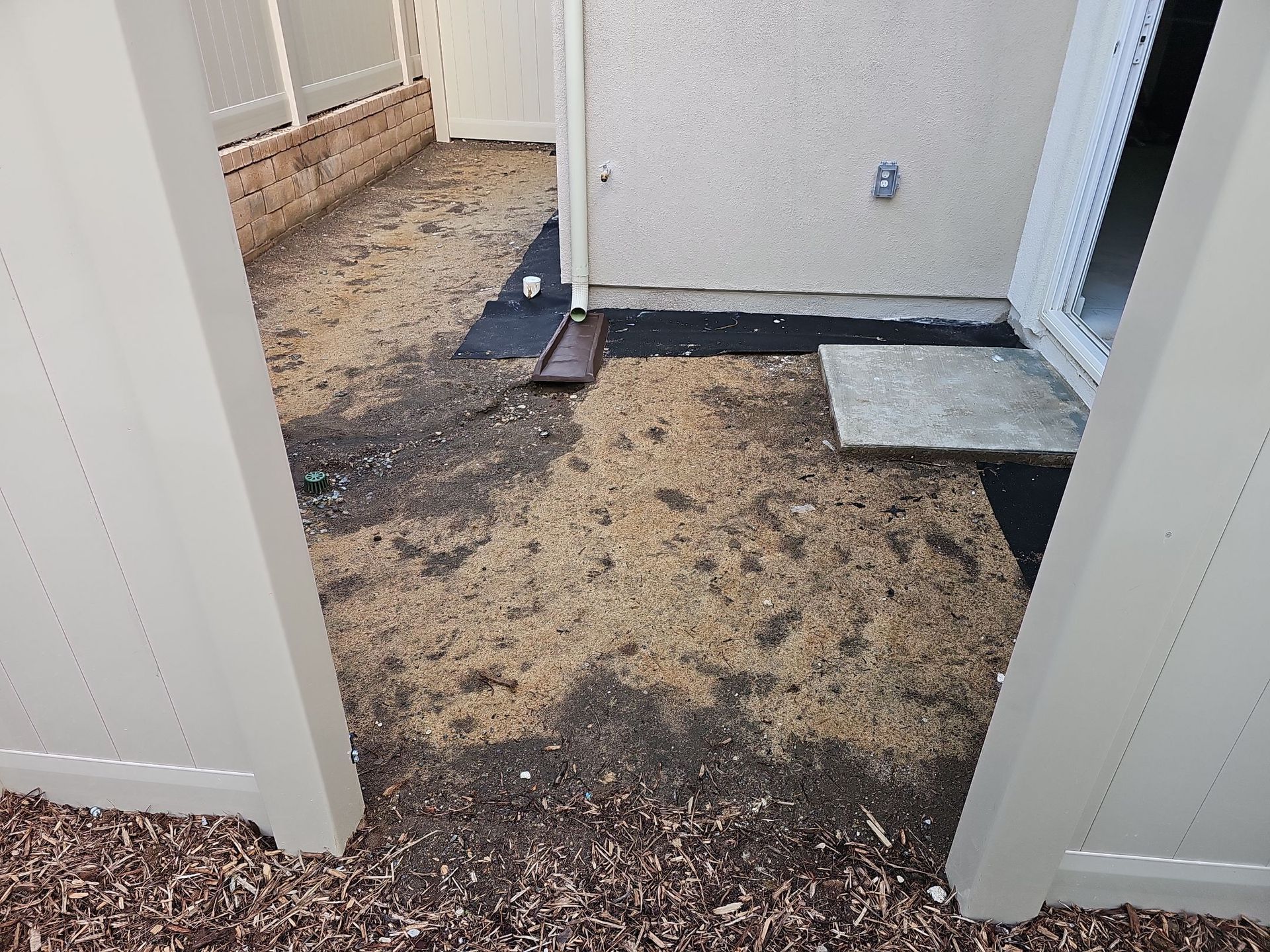 A courtyard with bare ground, some mulch, and a concrete patio slab.