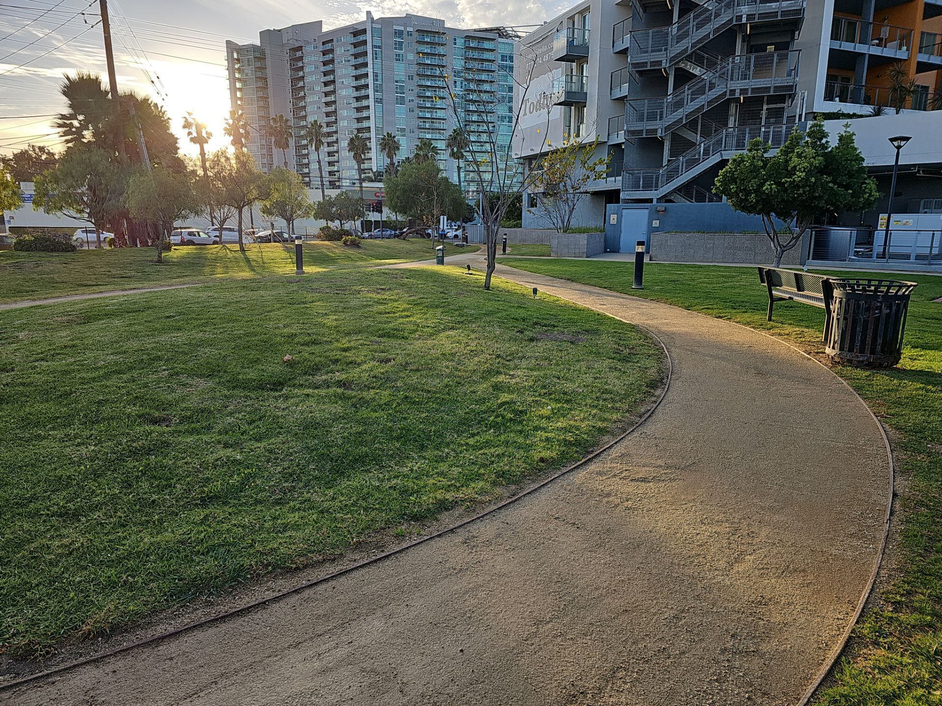 Curving path through a park with green grass and modern apartment buildings in the background.