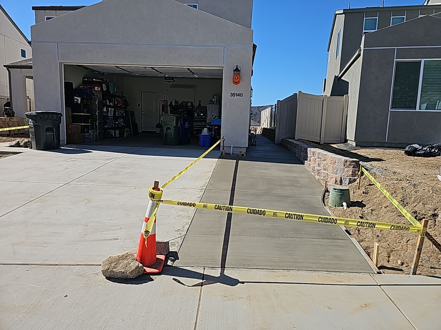 Concrete driveway with fresh cement path blocked by caution tape; house and garage in background.