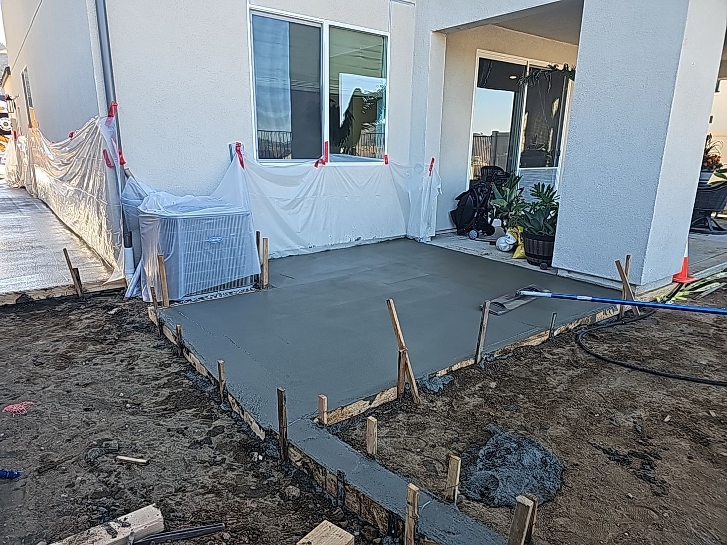 Newly poured concrete patio next to a house under construction; exposed wooden frame.