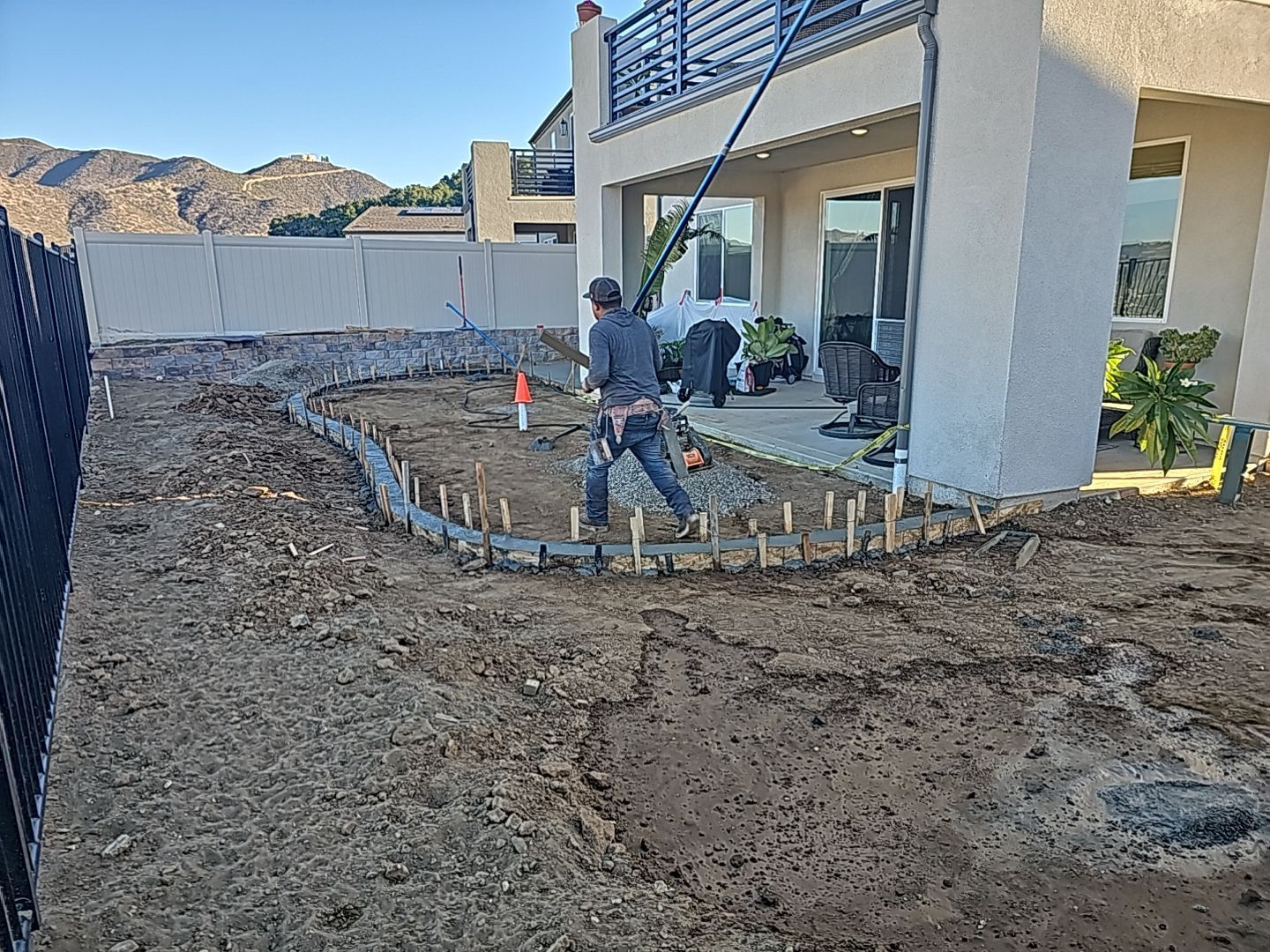 Construction workers building a garden bed in a backyard, beside a house, mountains in the distance.