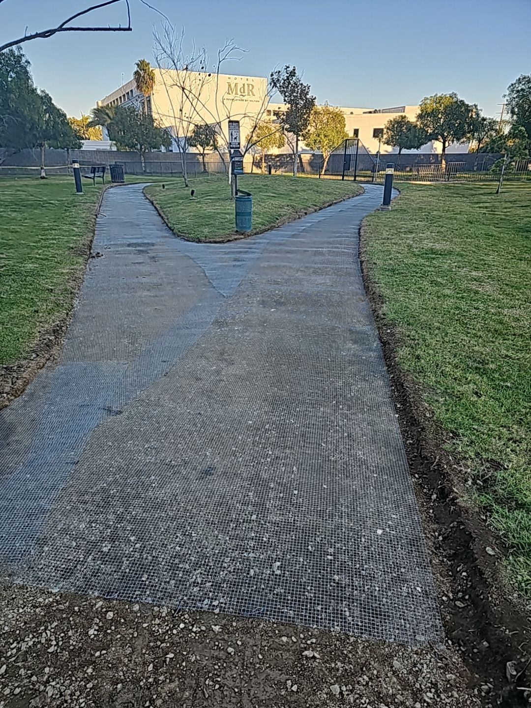 Forking paved path in a grassy park, leading towards a building.