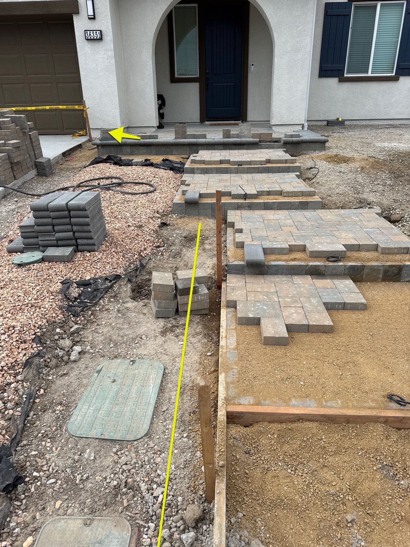 Construction of a paved walkway leading to a house entrance. Pavers, gravel, and steps are visible.