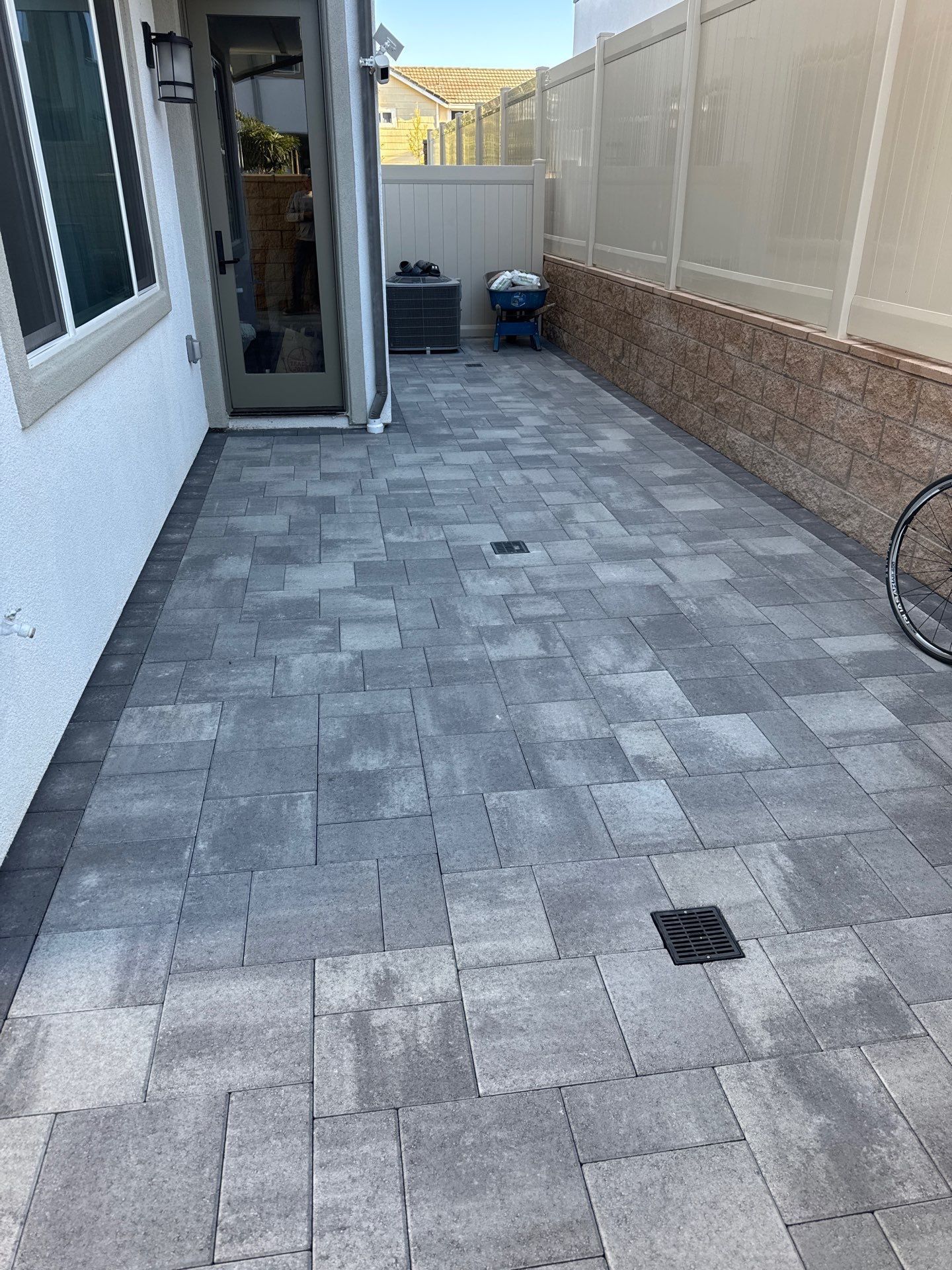 Patio with gray pavers, drainage, a door, and a white fence.
