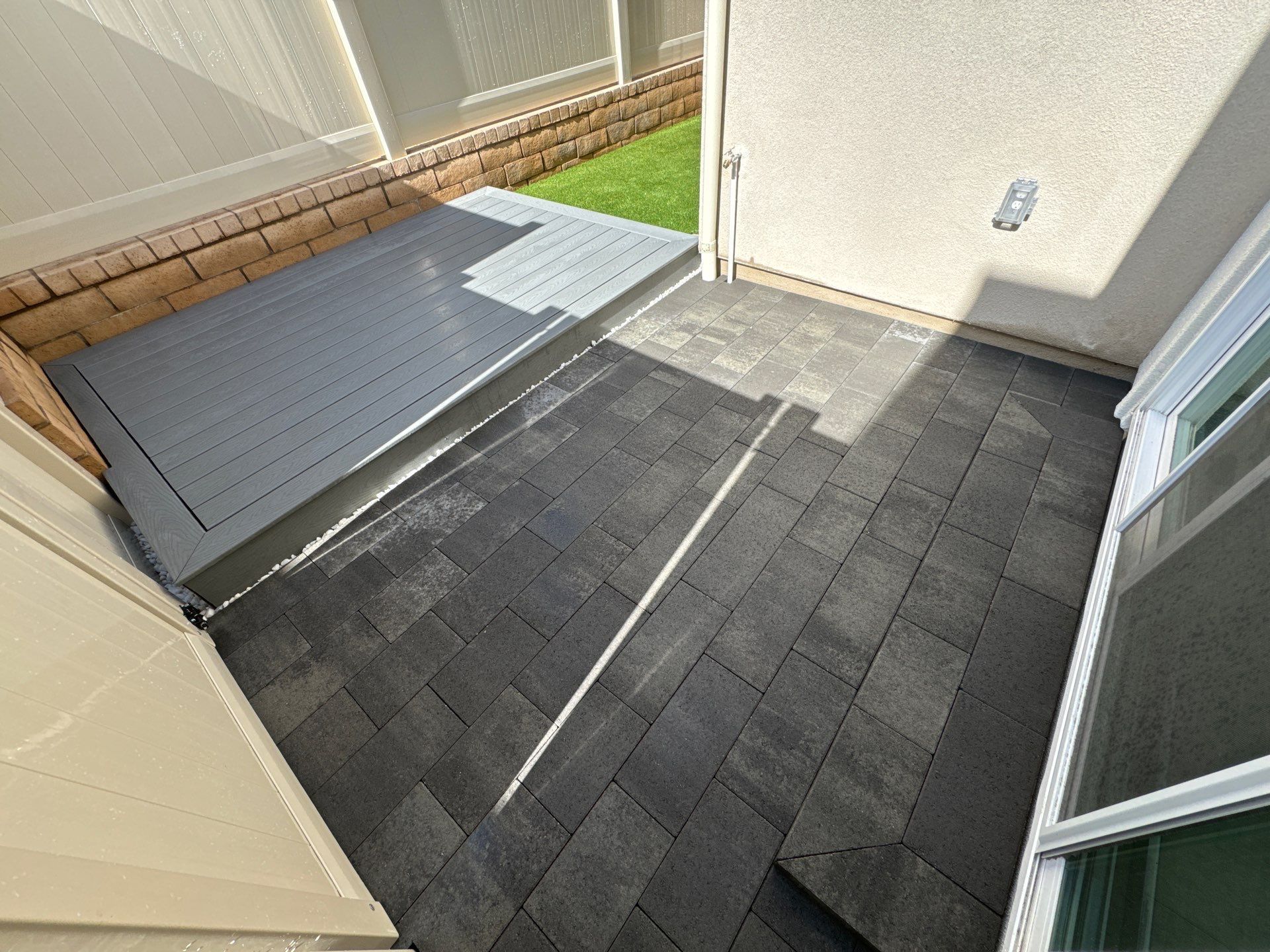 A small patio area with dark gray shingles, leading to a light gray covered area.