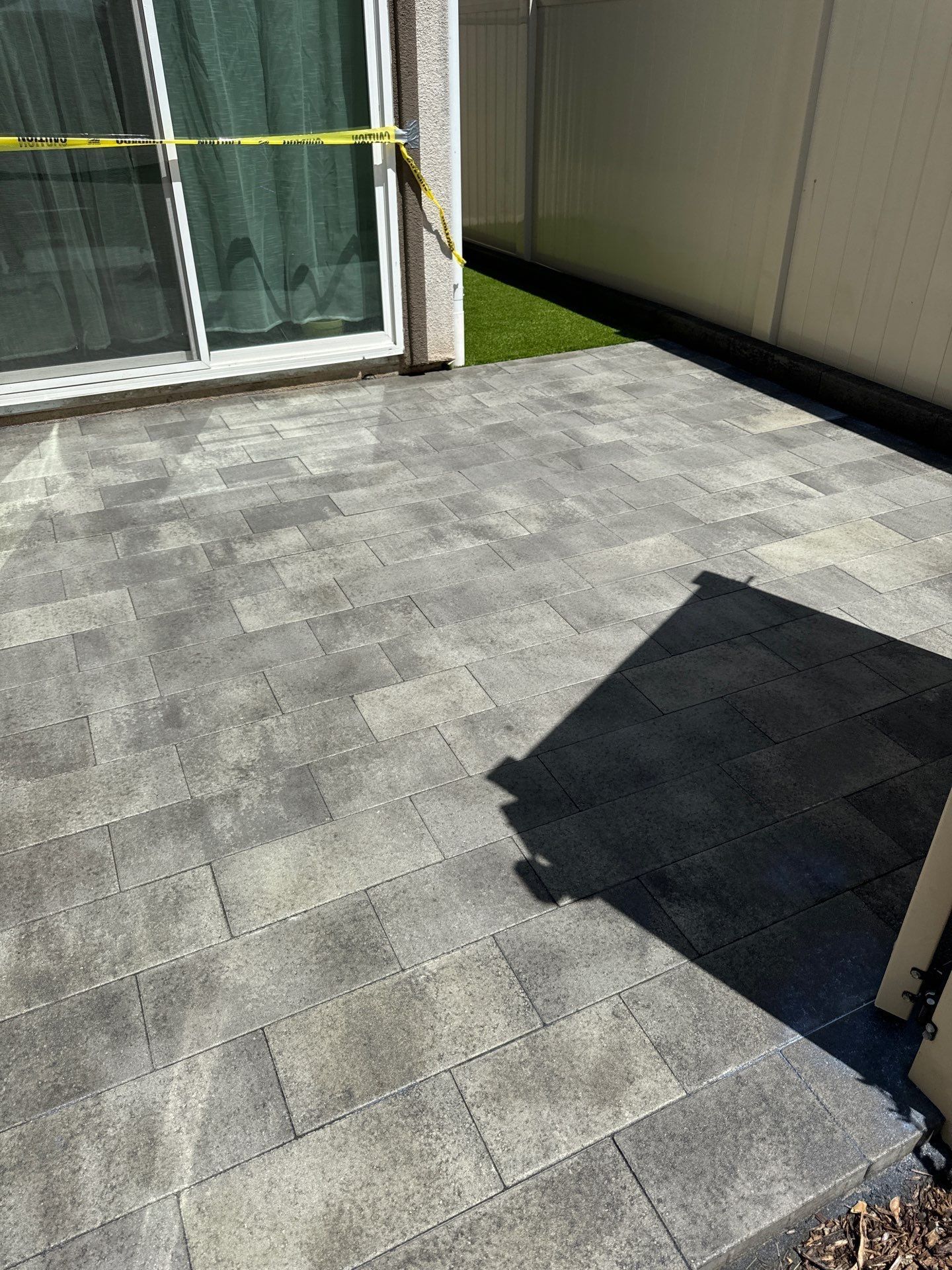 Patio paved with gray rectangular stones, next to a sliding glass door and artificial grass.