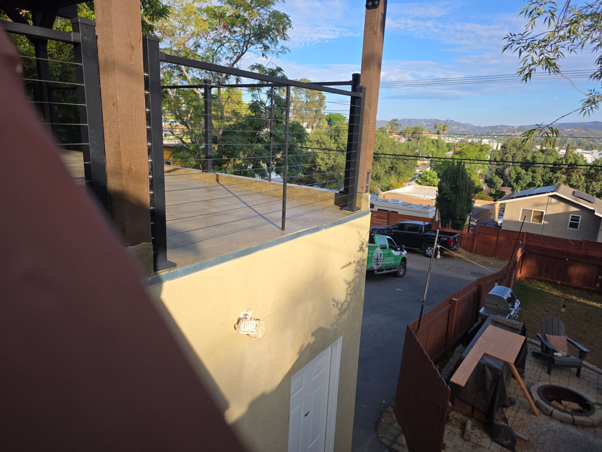 View from a balcony overlooking a residential street and hills, with a green truck visible.