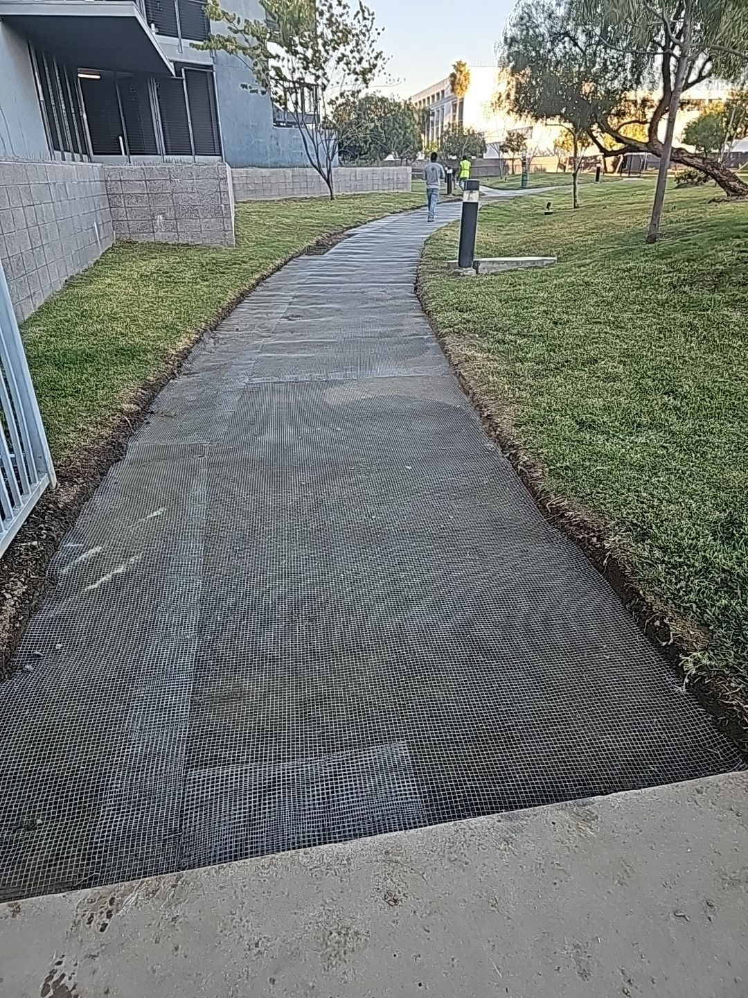 Pathway made of grid-like material curves through grassy area, leading toward buildings.