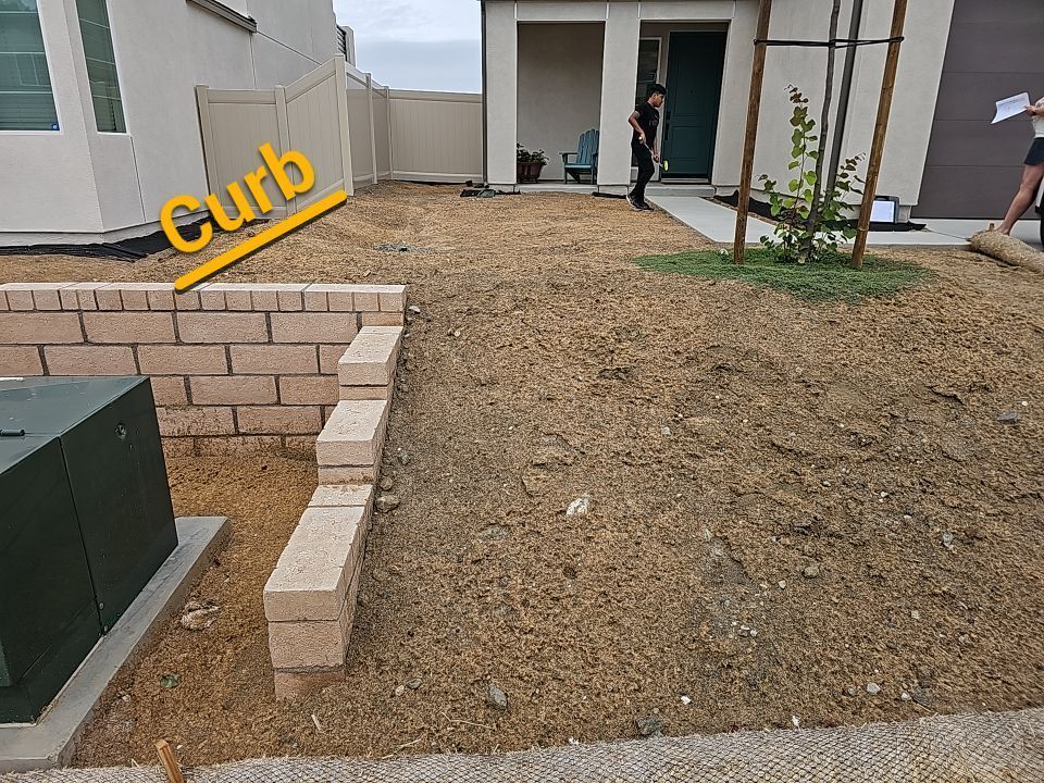 Front yard with brick retaining wall, dirt ground, small tree, and utility box. Person standing near door.