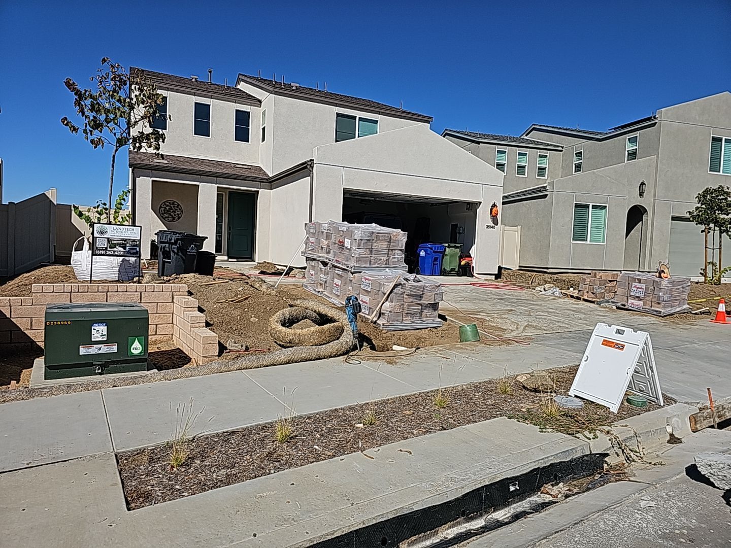 New home under construction; beige exterior, open garage. Unfinished landscaping, materials in driveway.