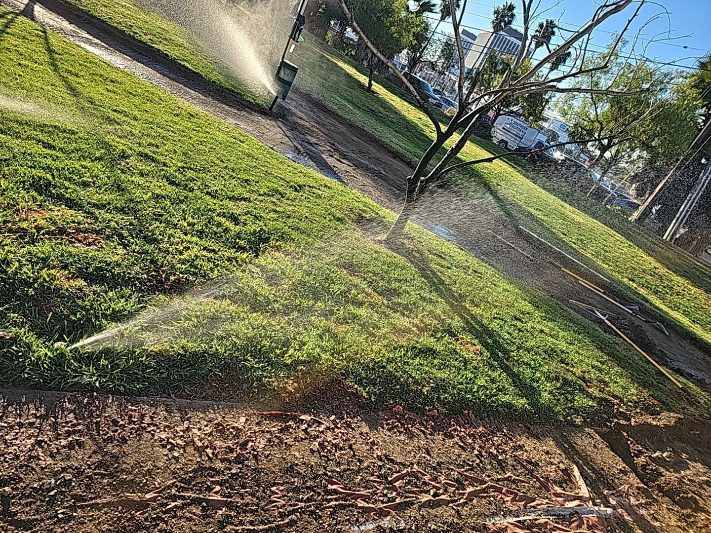 Sprinklers watering a green grassy hillside in a sunny outdoor setting.