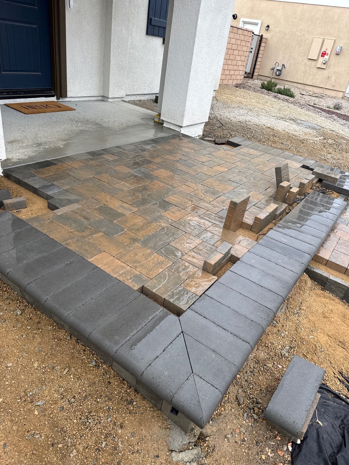 Construction of a patio with gray border and brick pavers in front of a house.