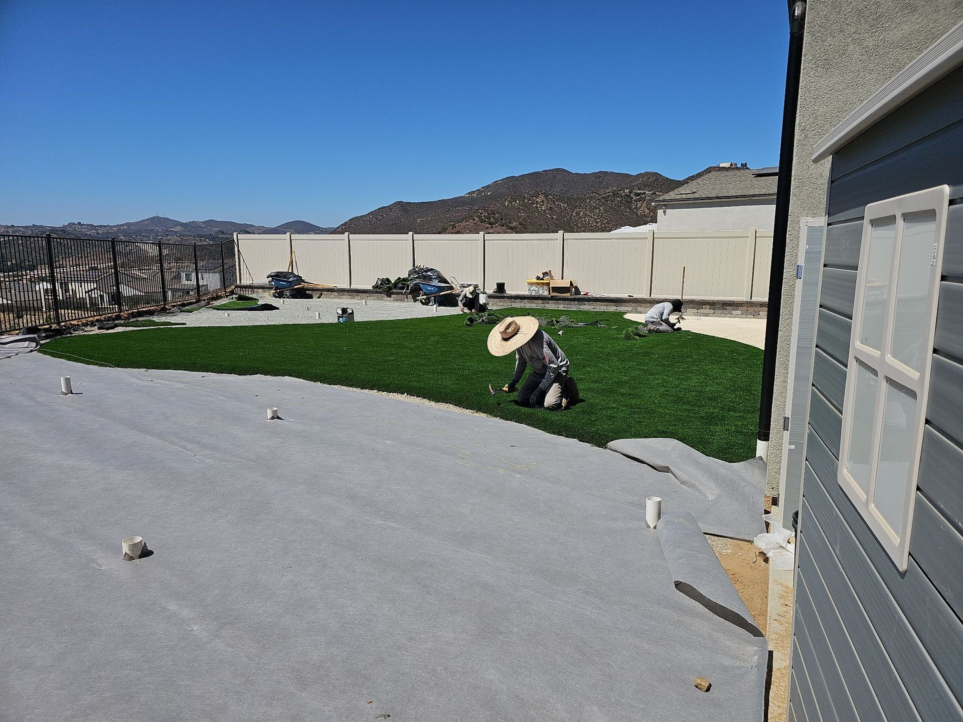 Workers installing artificial turf in a backyard on a sunny day.