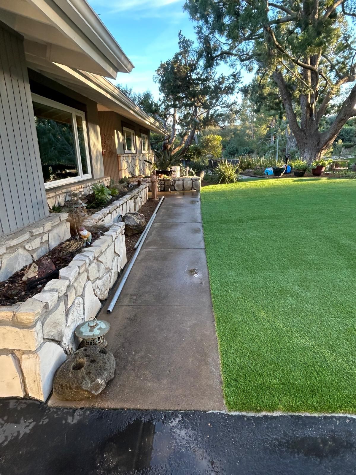 Exterior view of a house with a concrete walkway, stone planter, and artificial green lawn.
