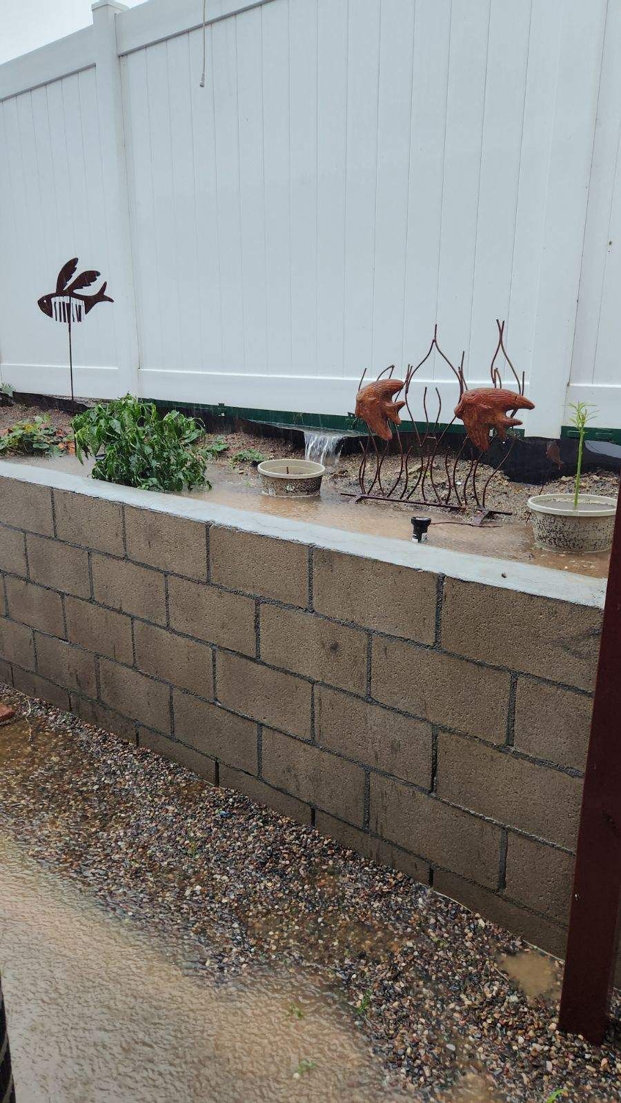 A retaining wall with a garden bed, gray wall, and white fence in a yard.