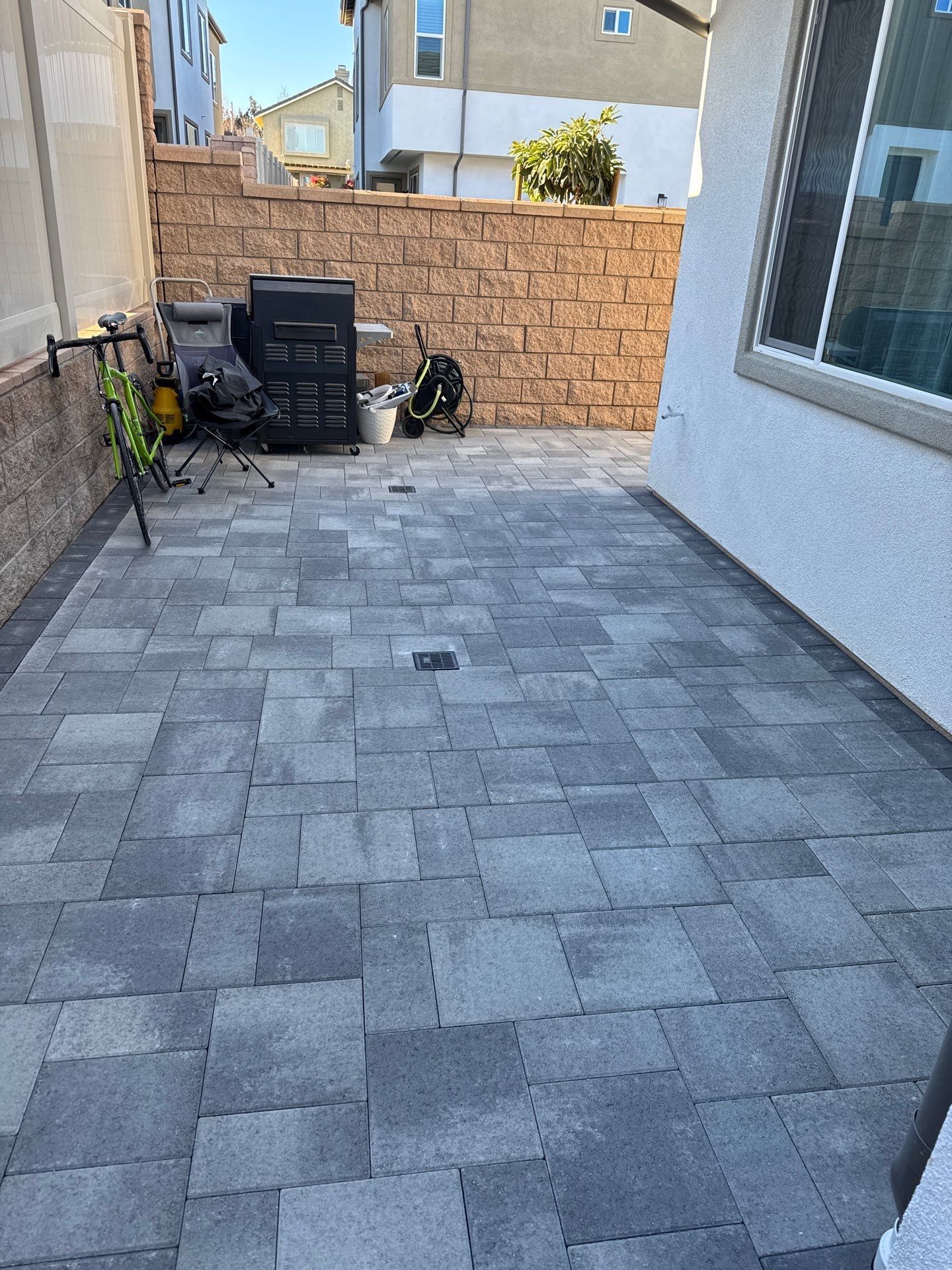 Patio with gray pavers, brick wall, and grill. House in the background.