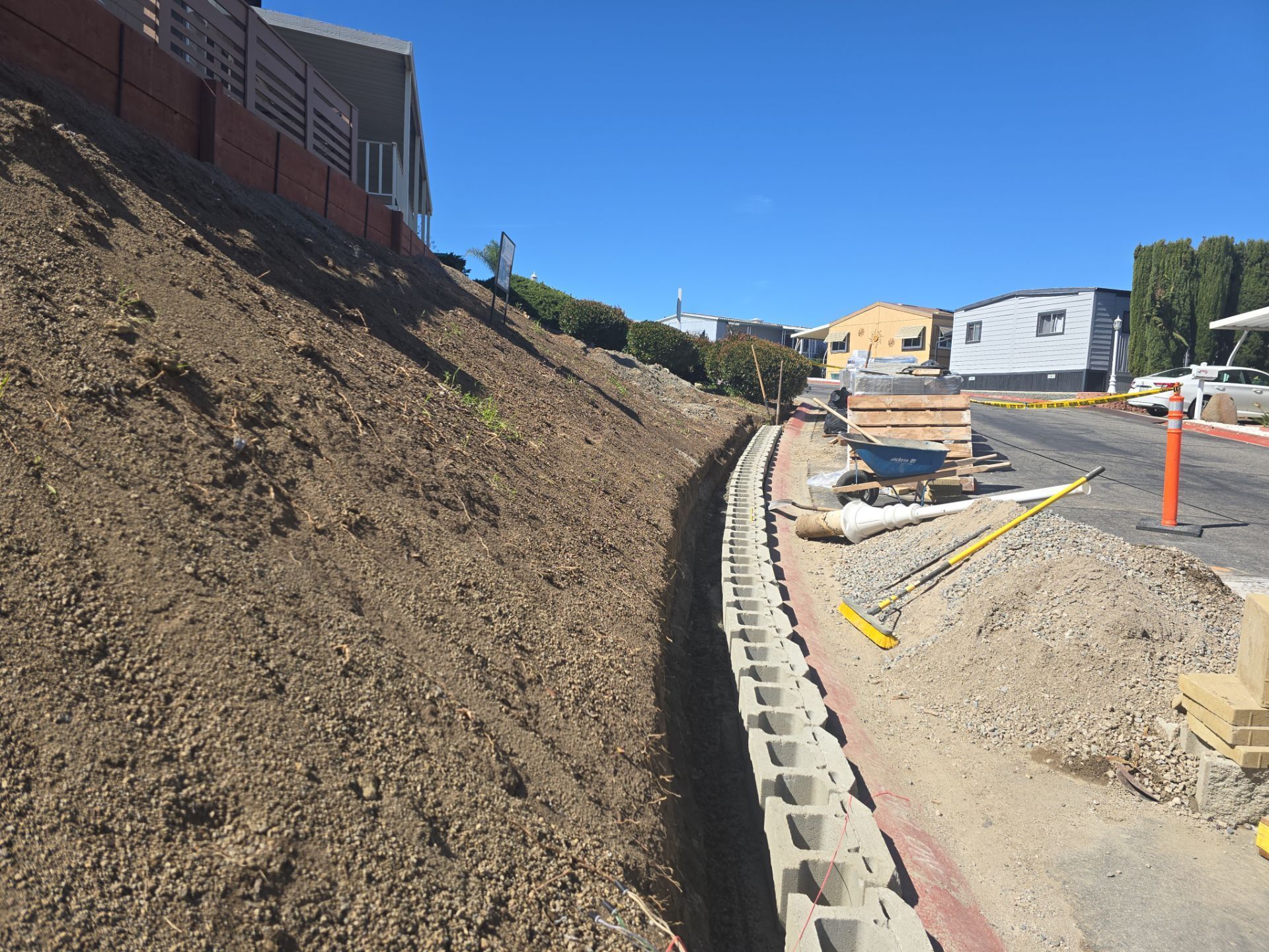 Construction site with retaining wall made of concrete blocks along a hillside next to a road.