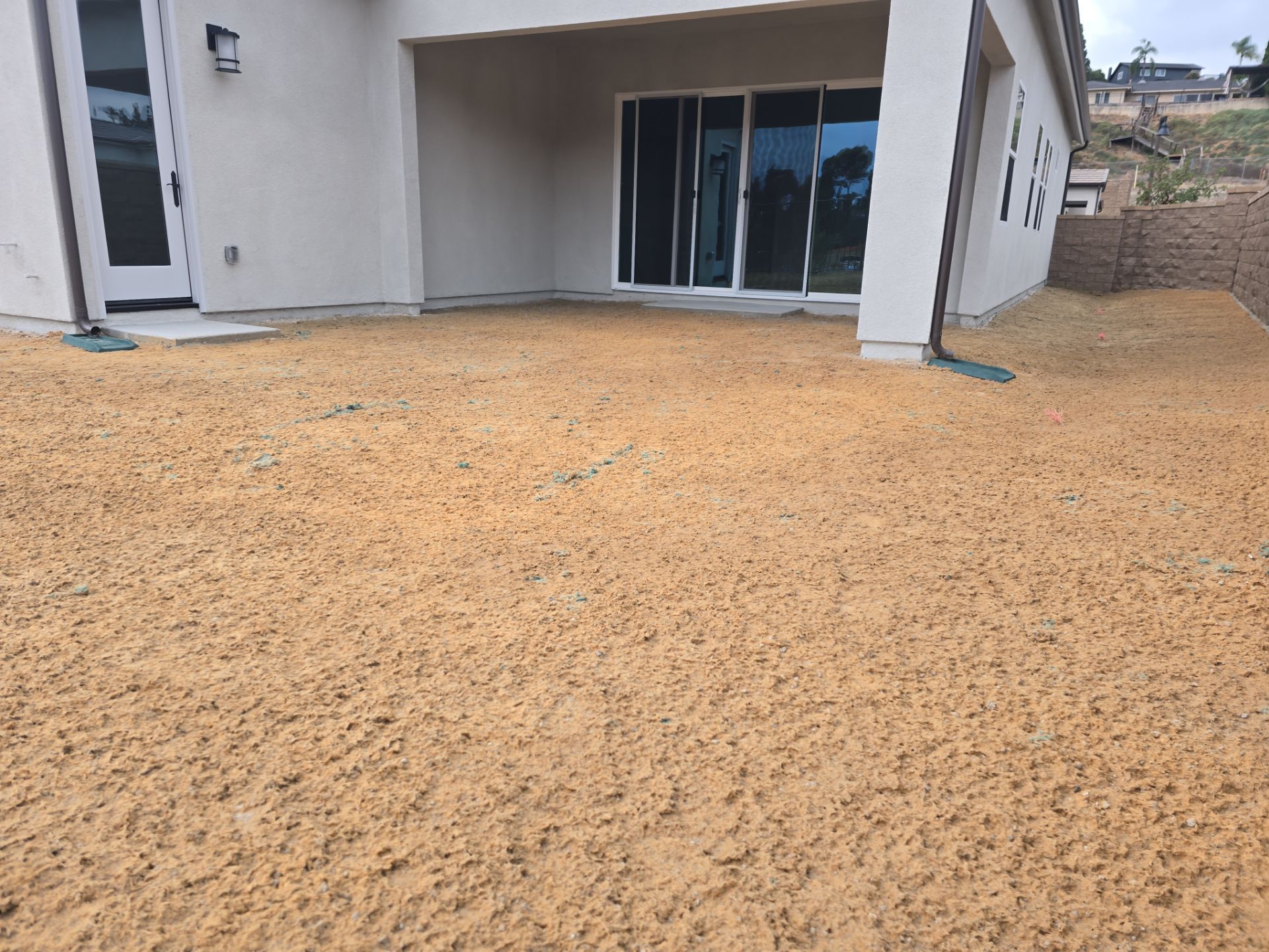 Backyard covered in tan gravel, next to a house with glass sliding doors and an overhanging patio.