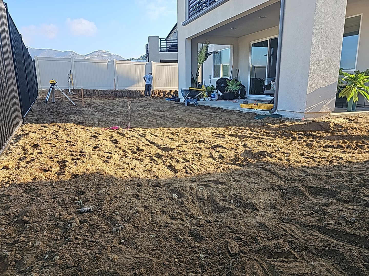 Yard being prepared for landscaping next to a two-story house. Workers are present, and soil is visible.