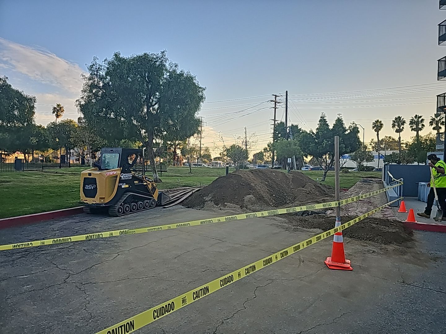Construction site with small excavator, dirt pile, caution tape, and worker.