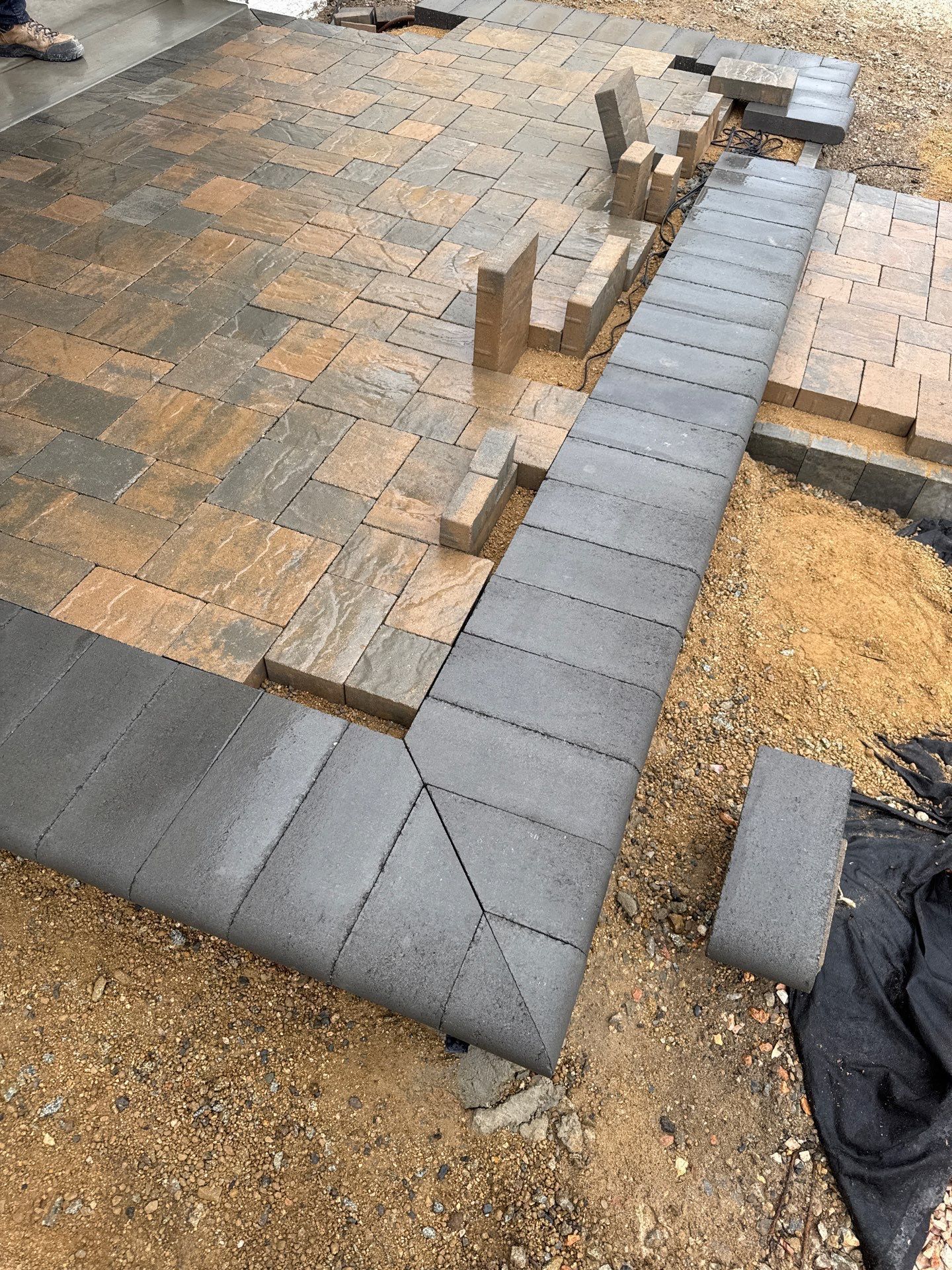 Construction of a brick patio with gray border bricks and patterned pavers.