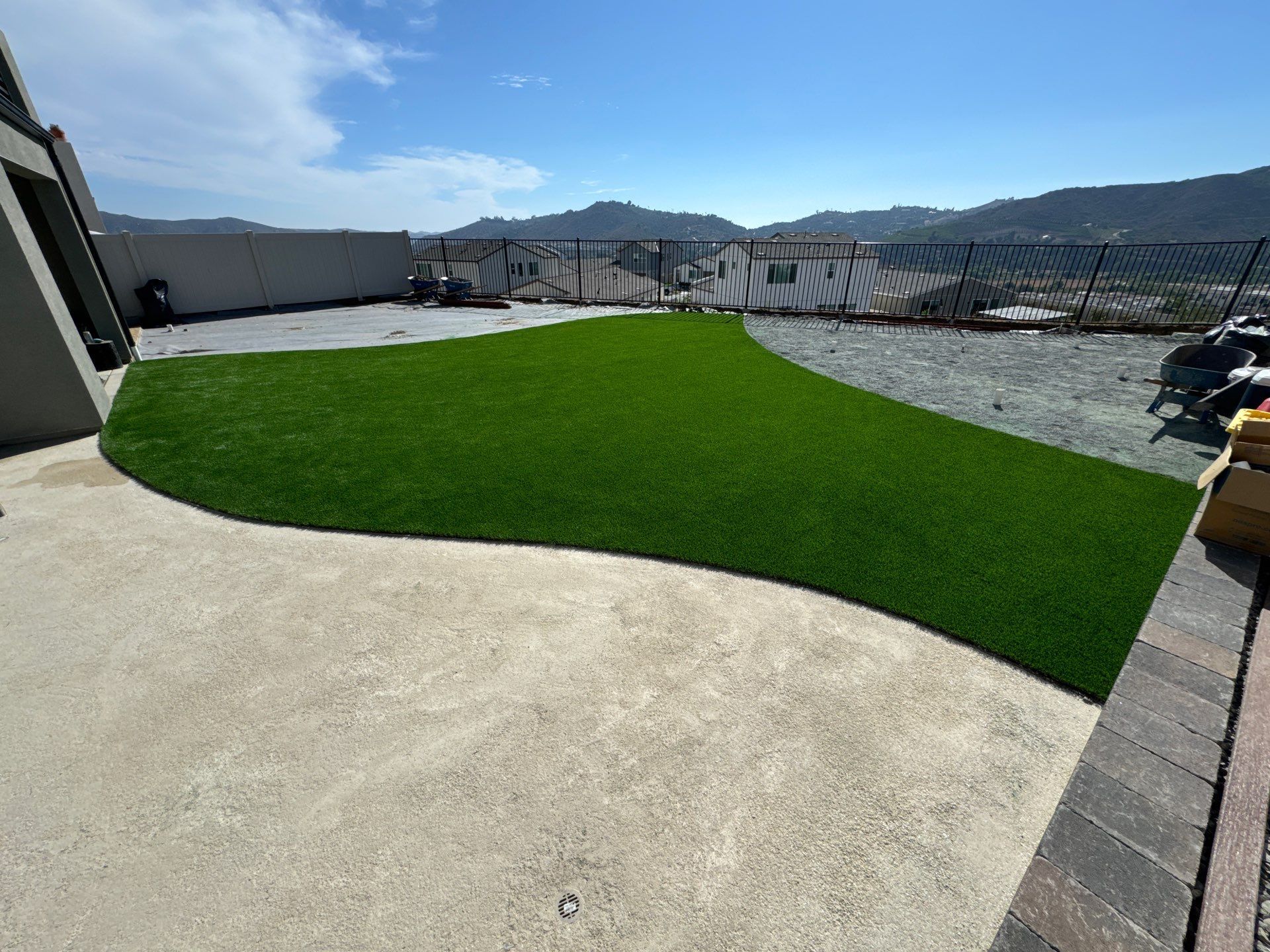 Artificial turf lawn on a concrete patio with a mountainous backdrop under a blue sky.