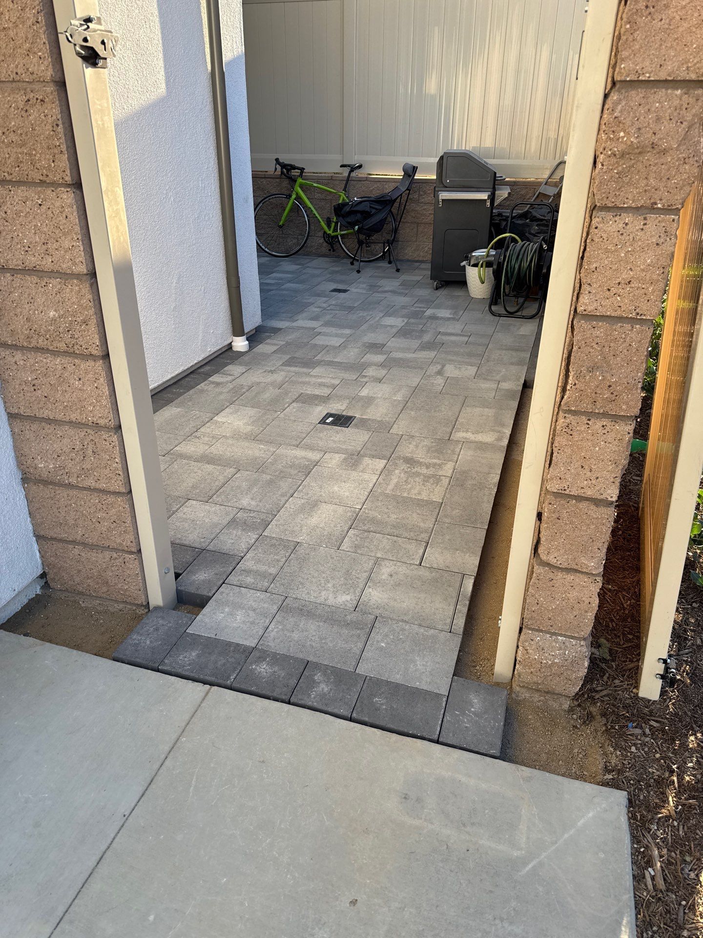 Brick entrance with gray paver walkway and ramp leading to a patio with a bike and grill.