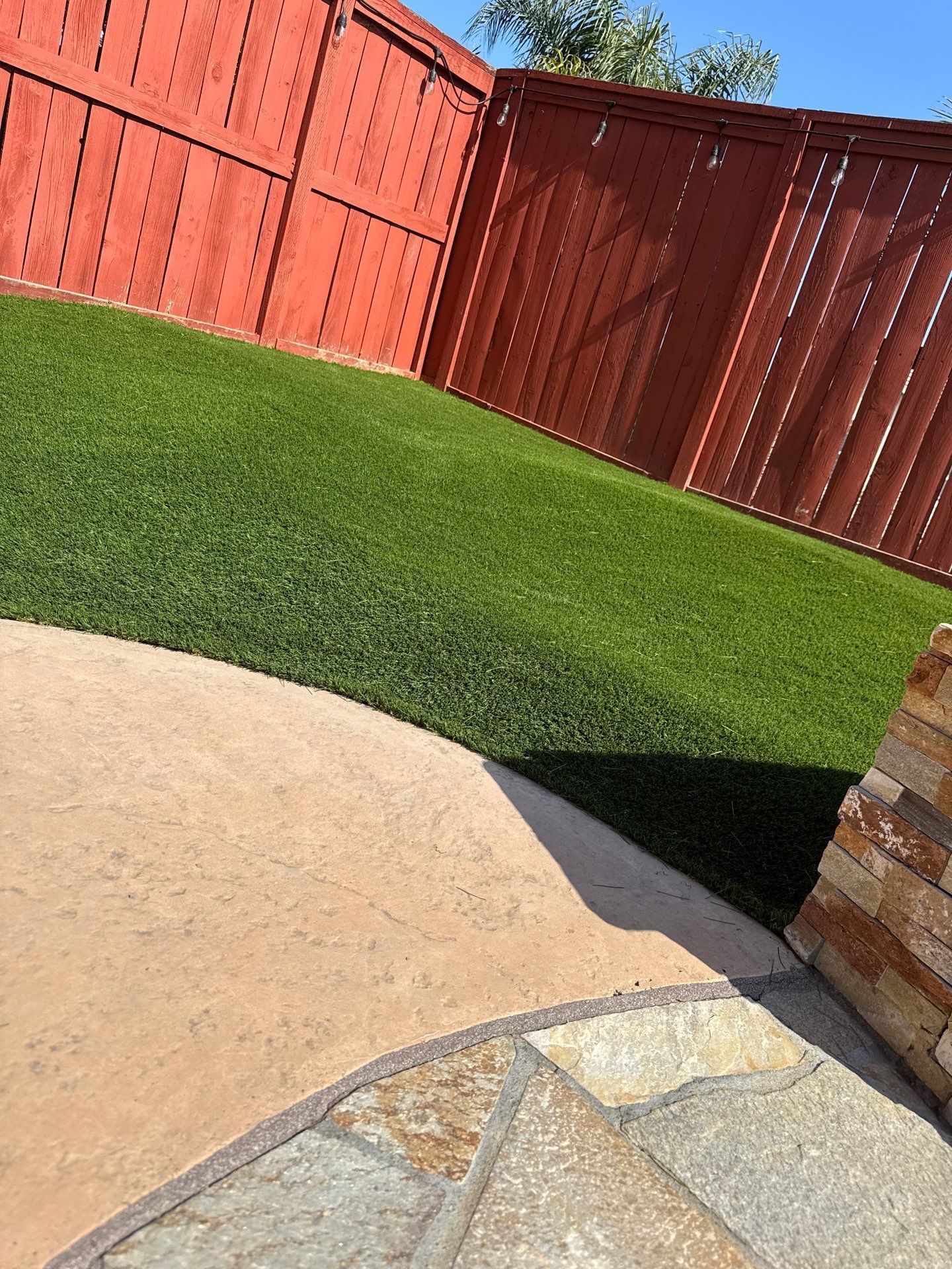 Green artificial turf in backyard with red fence and concrete patio.