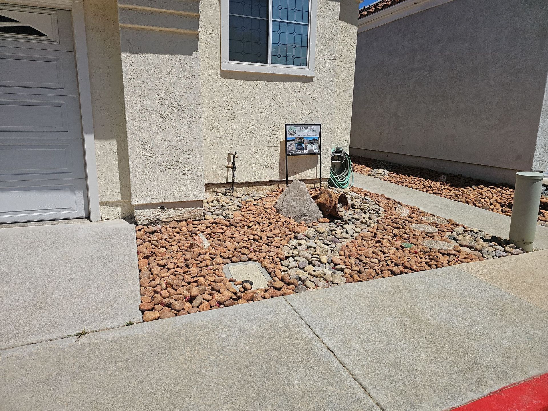 Exterior of a house with gravel landscaping. Beige stucco wall, small window, and concrete sidewalk.
