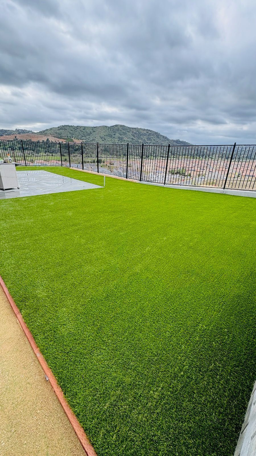 Green artificial turf with a mountain view under a cloudy sky.
