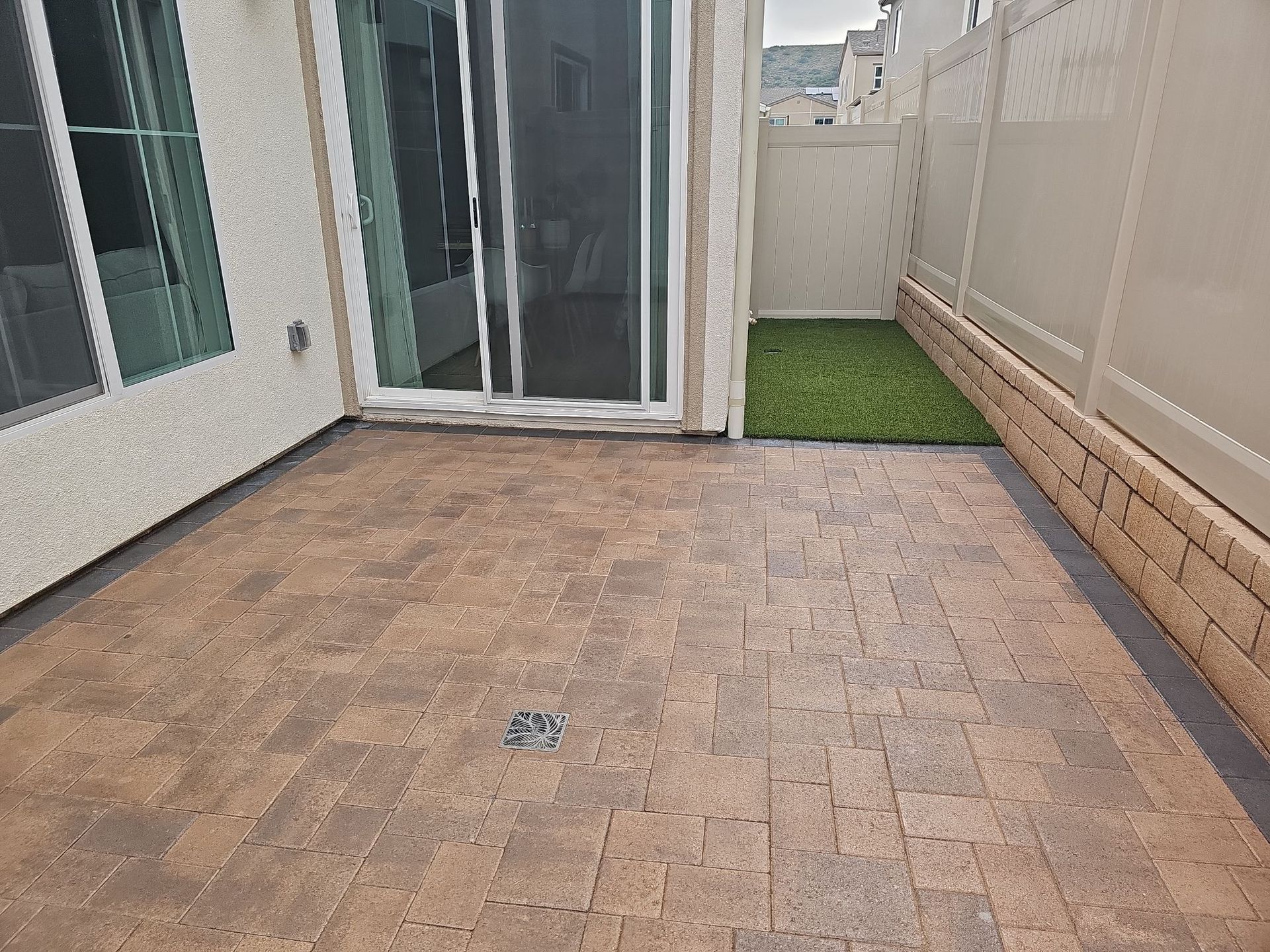 Patio with brick pavers, sliding glass door, artificial grass, and beige fence.
