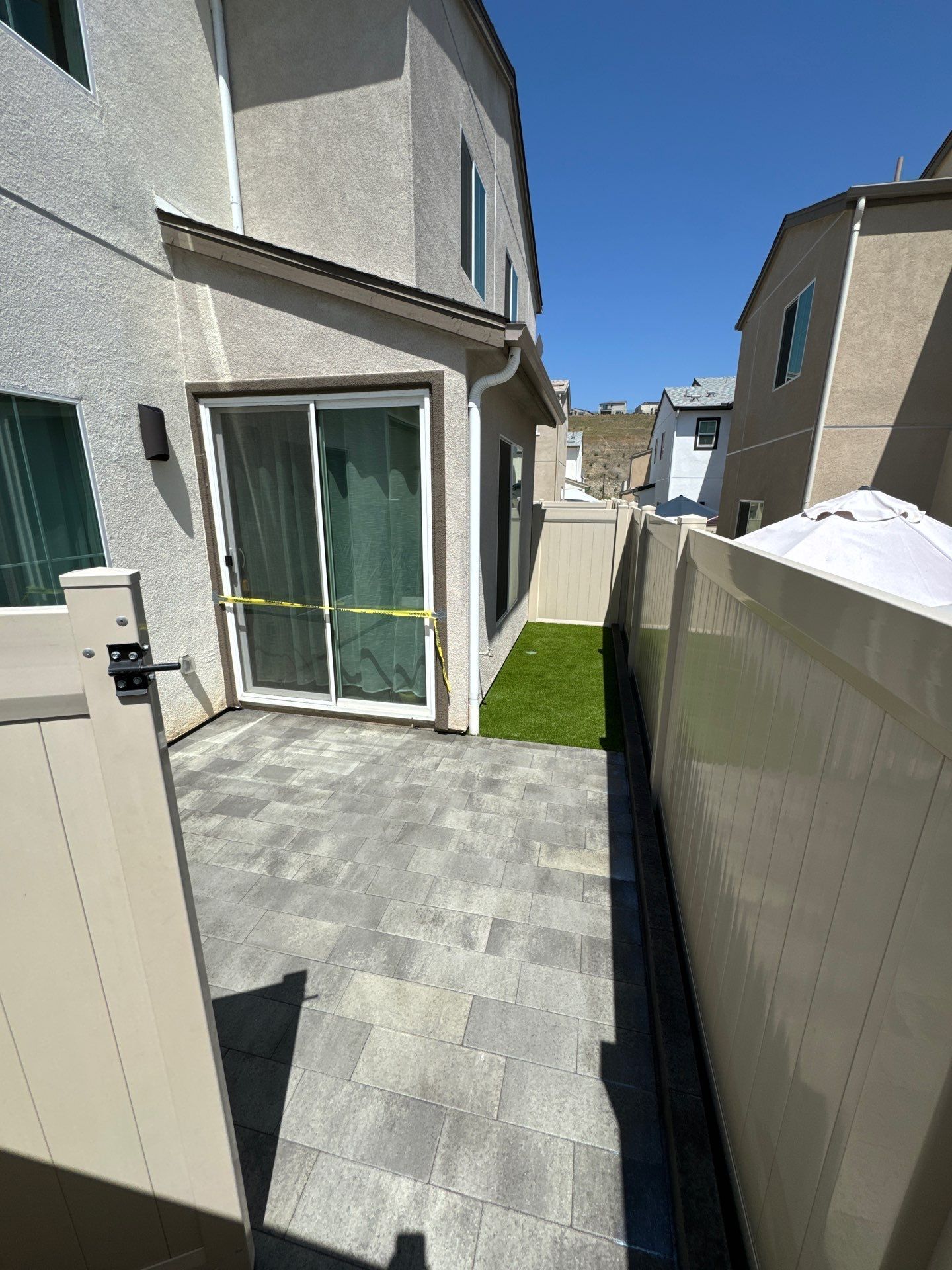 Patio with gray pavers, sliding glass door, small artificial turf, and beige fences.