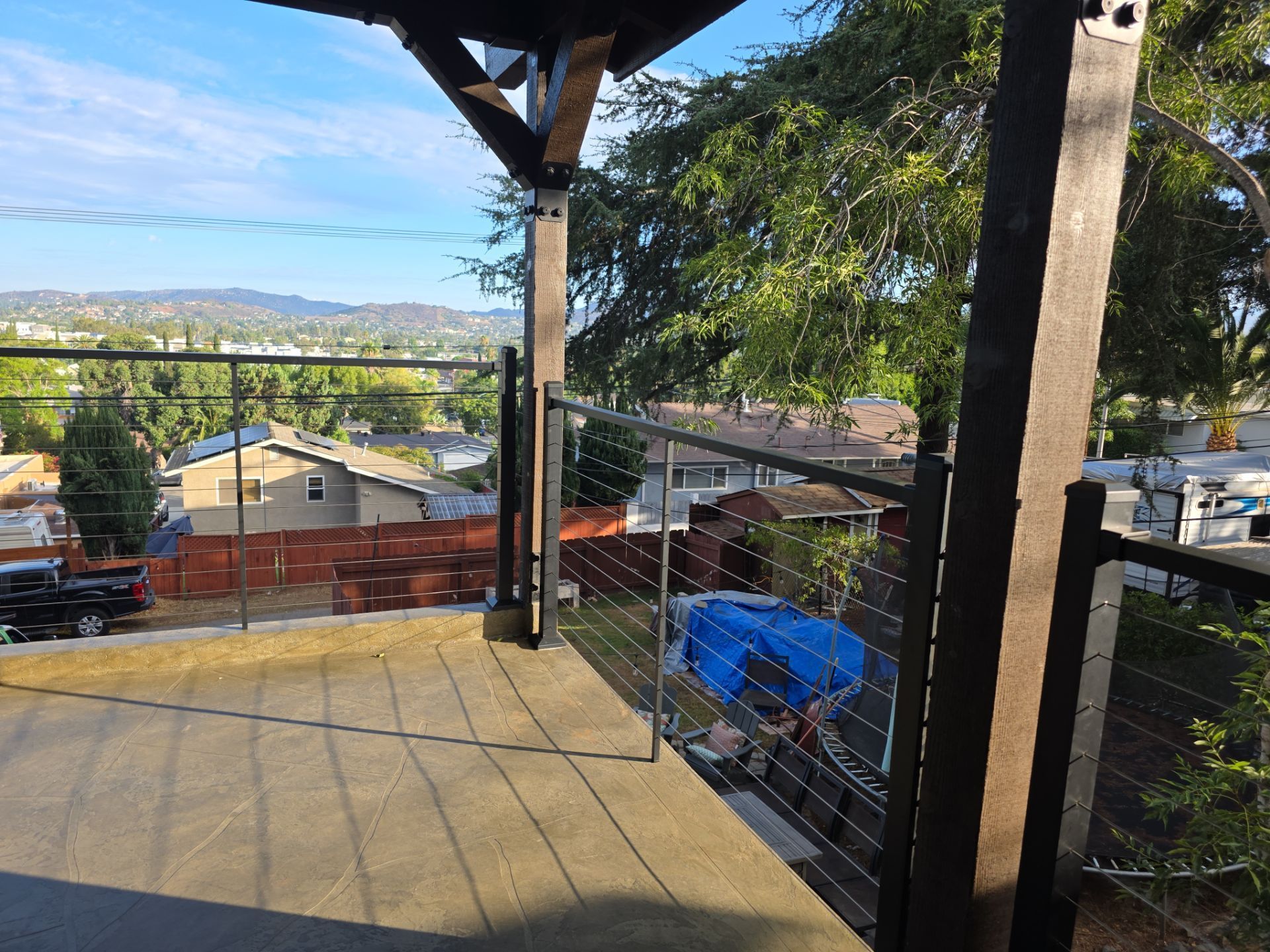 Deck with cable railing and cityscape view. Brown posts, gray deck, blue tarp.