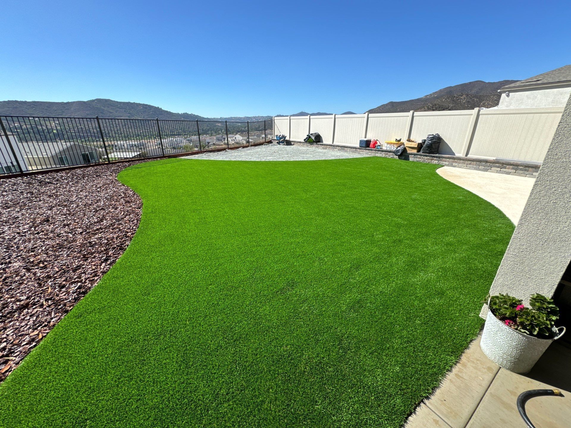 Backyard with green artificial turf, rock border, fence, and clear sky.